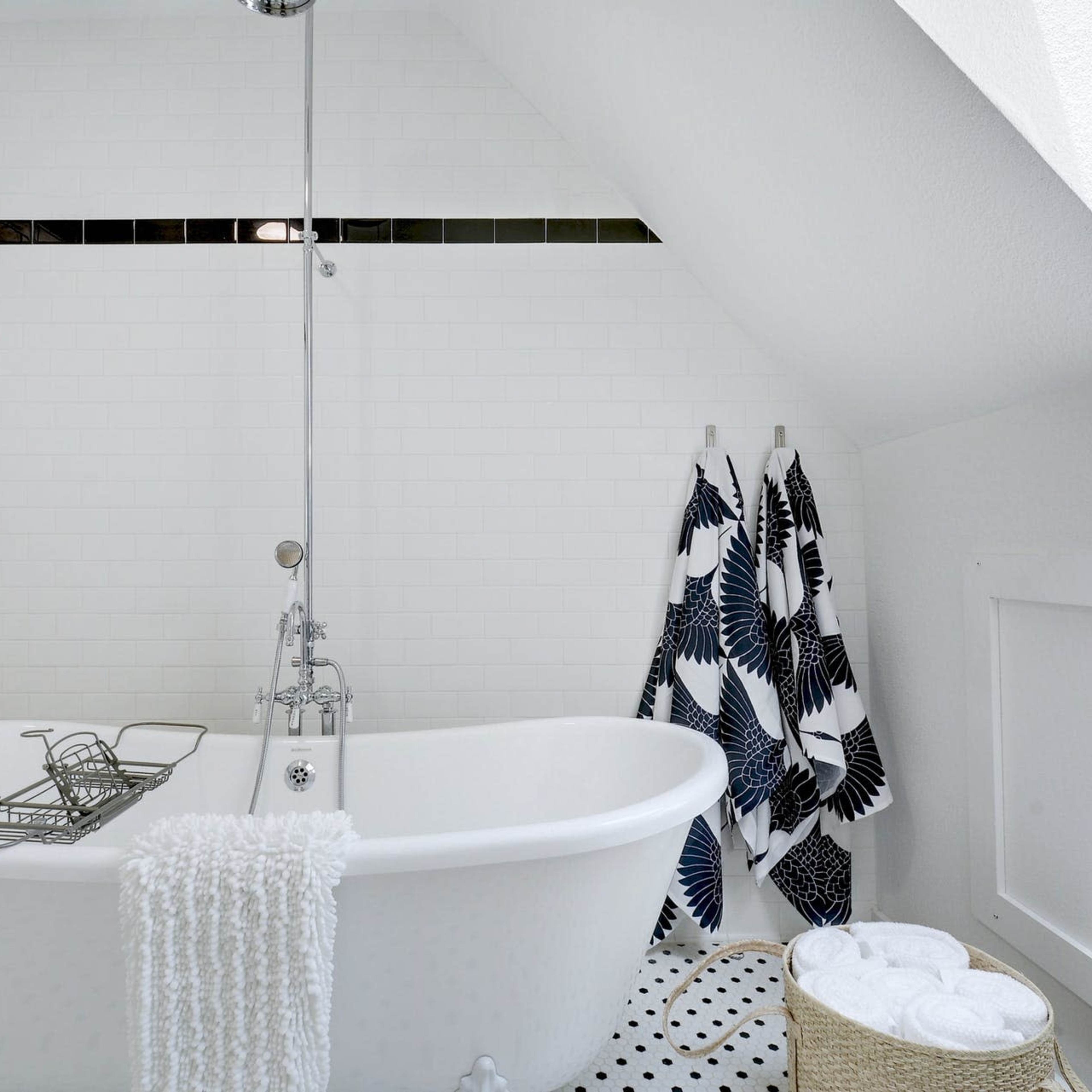 A modern bathroom featuring a freestanding bathtub, a shower fixture, white tiled walls, and neatly arranged towels.