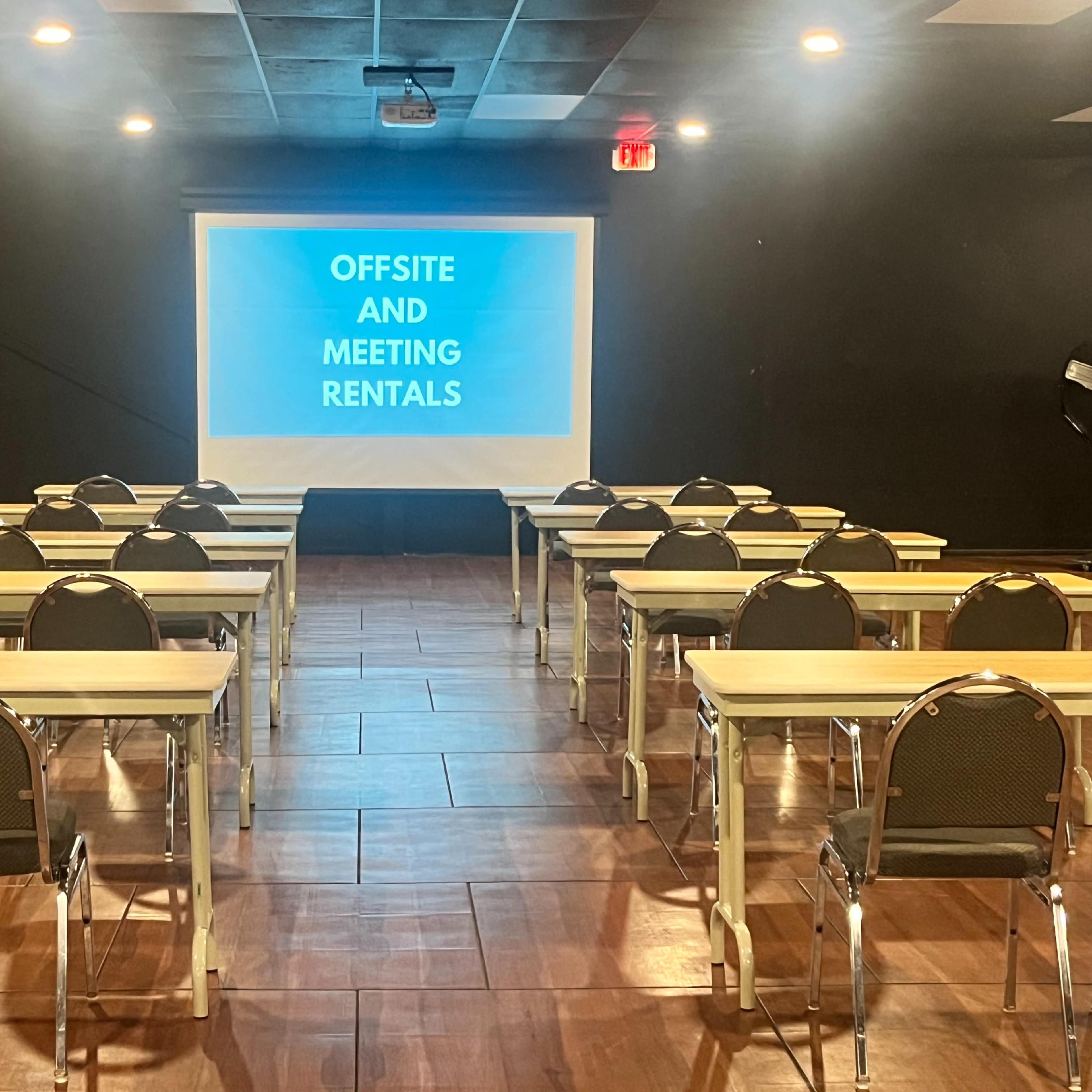 A classroom is set up with rows of tables and chairs facing a projector screen displaying "Offsite and Meeting Rentals."