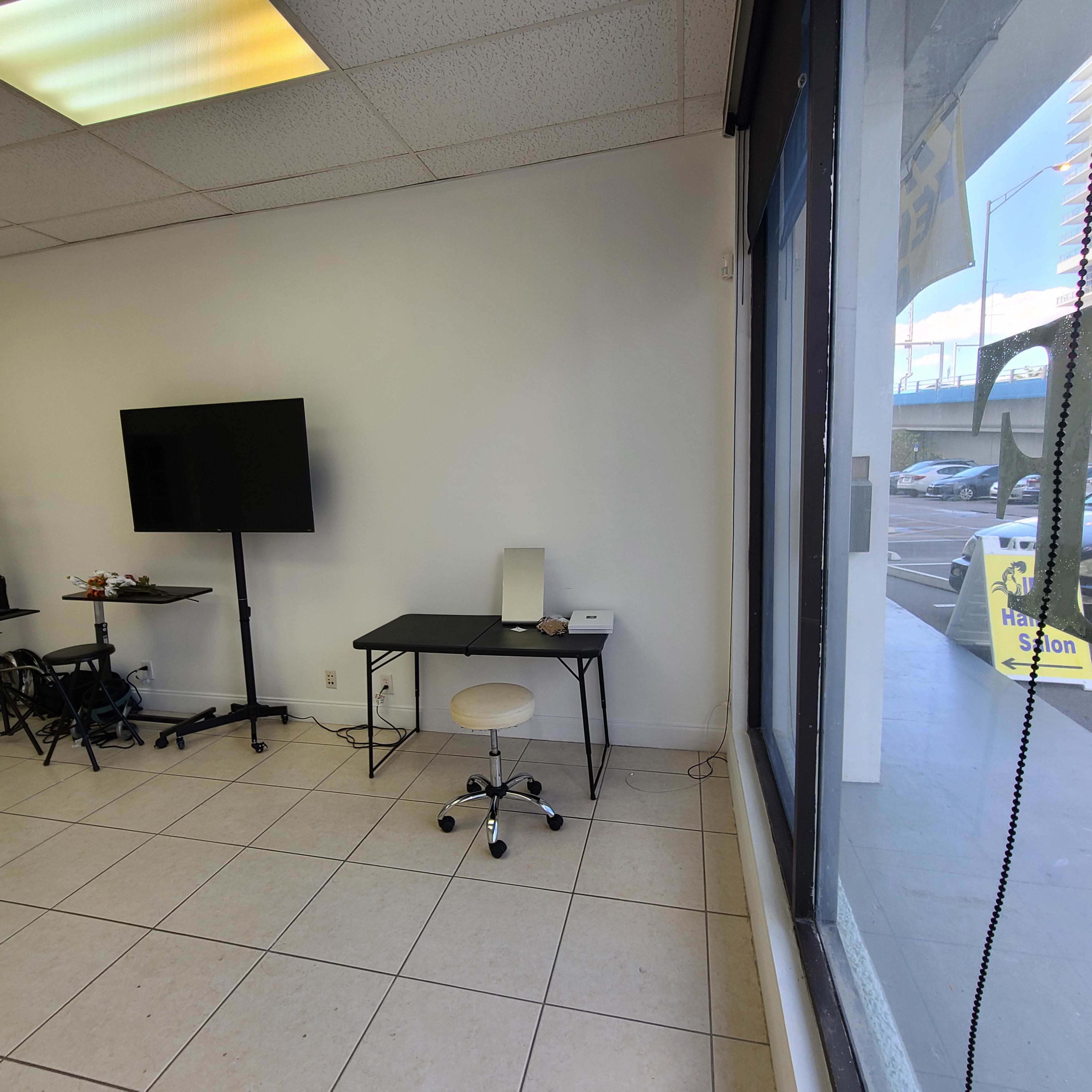 A minimalist office space with a black desk and chair positioned near a large window, along with a television screen on a stand.