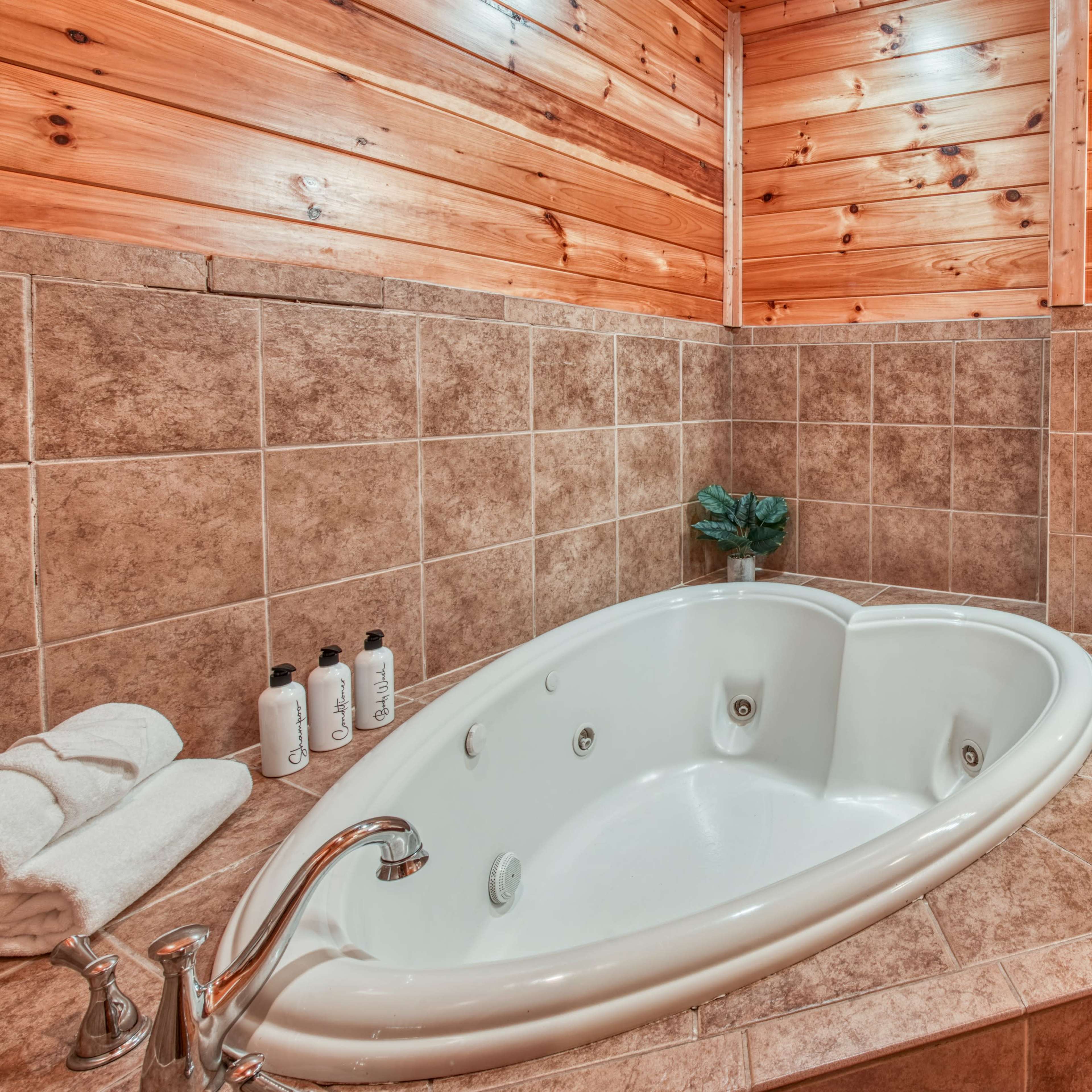 A bathroom featuring a jetted bathtub, stone tile walls, and wooden paneling, along with a sink area and mirrored cabinet.