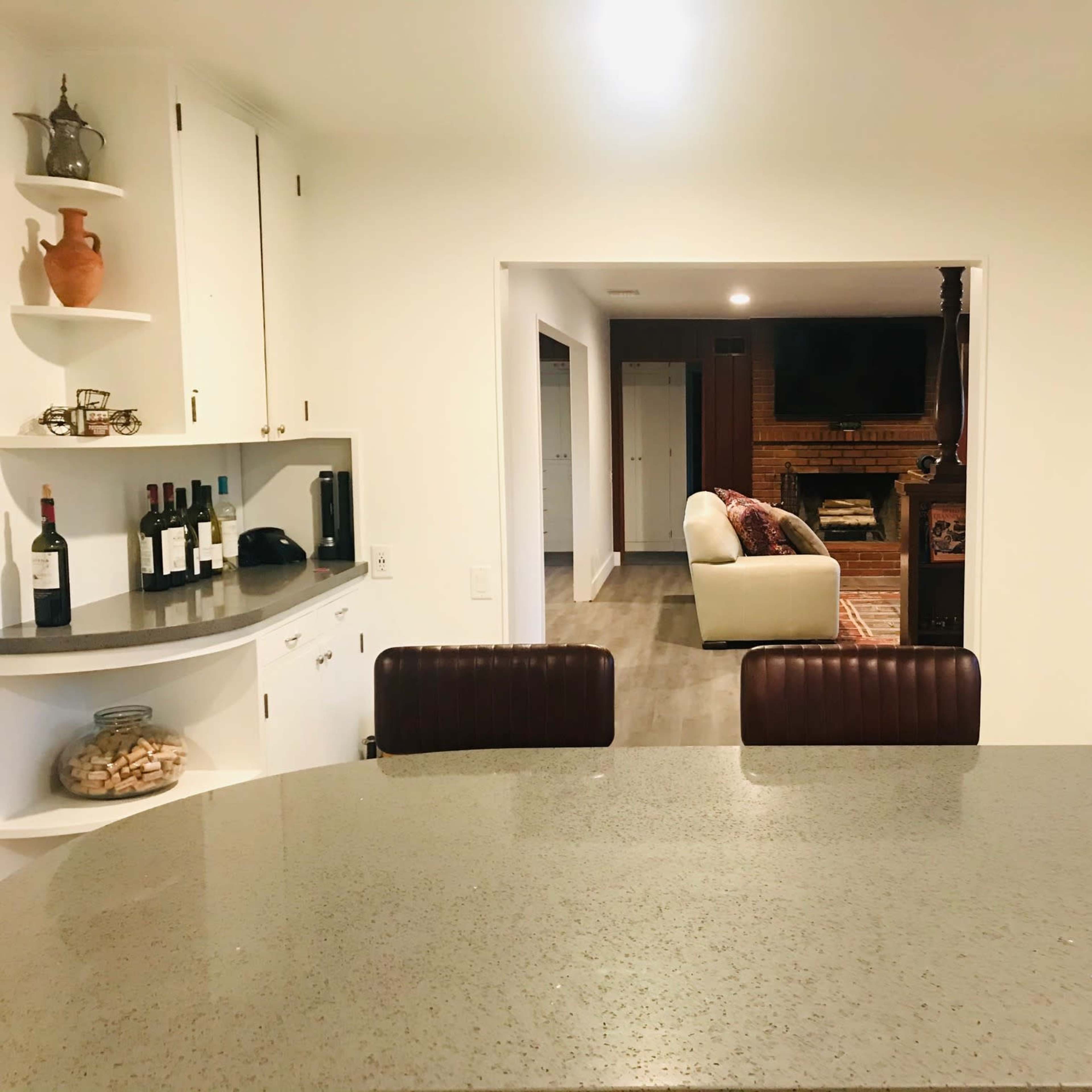 A modern kitchen features a bar area with seating that opens into a living room with a fireplace and comfortable seating.