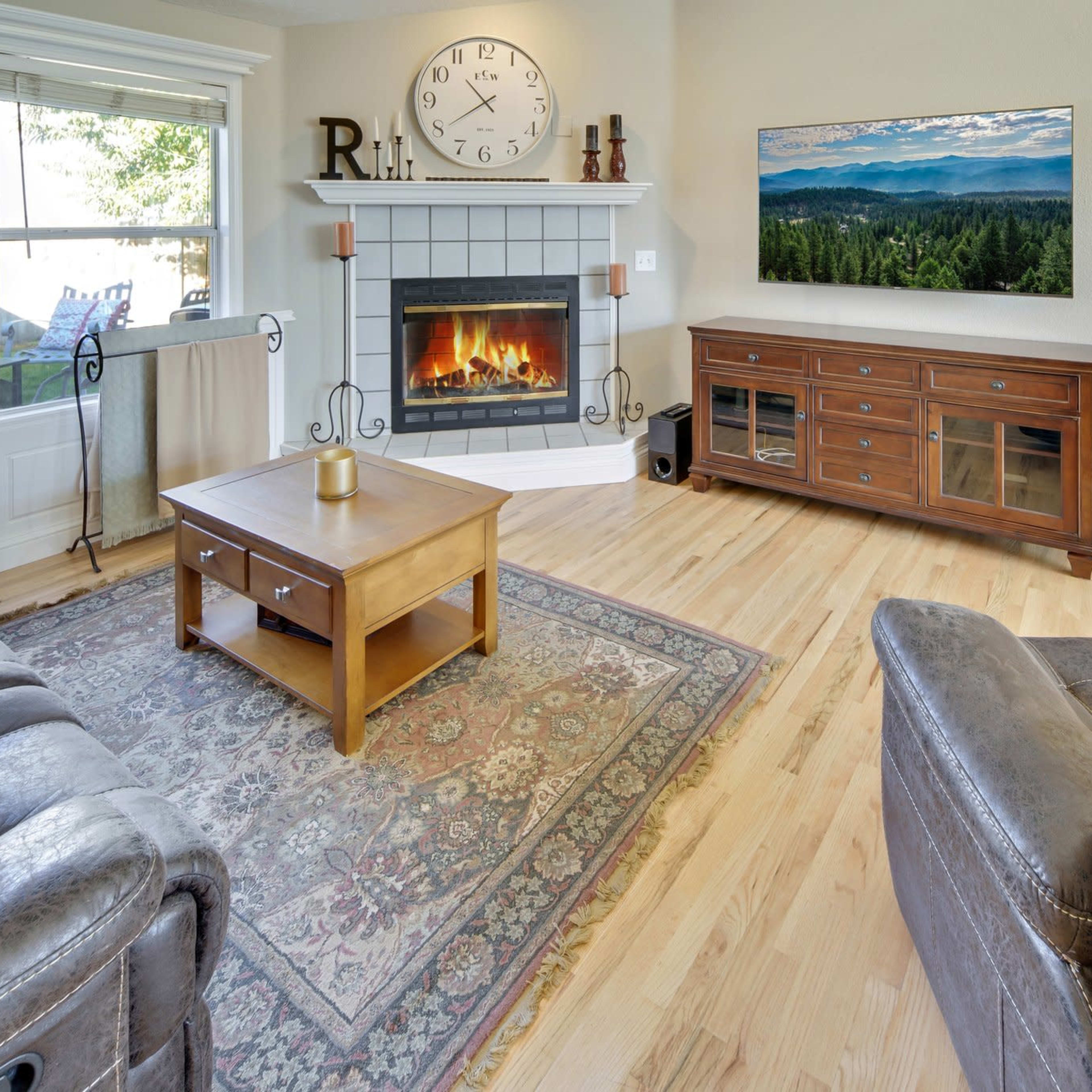 The living room features a gray fireplace with a wooden mantel, a coffee table in front, and a large television mounted on the wall above a wooden console.