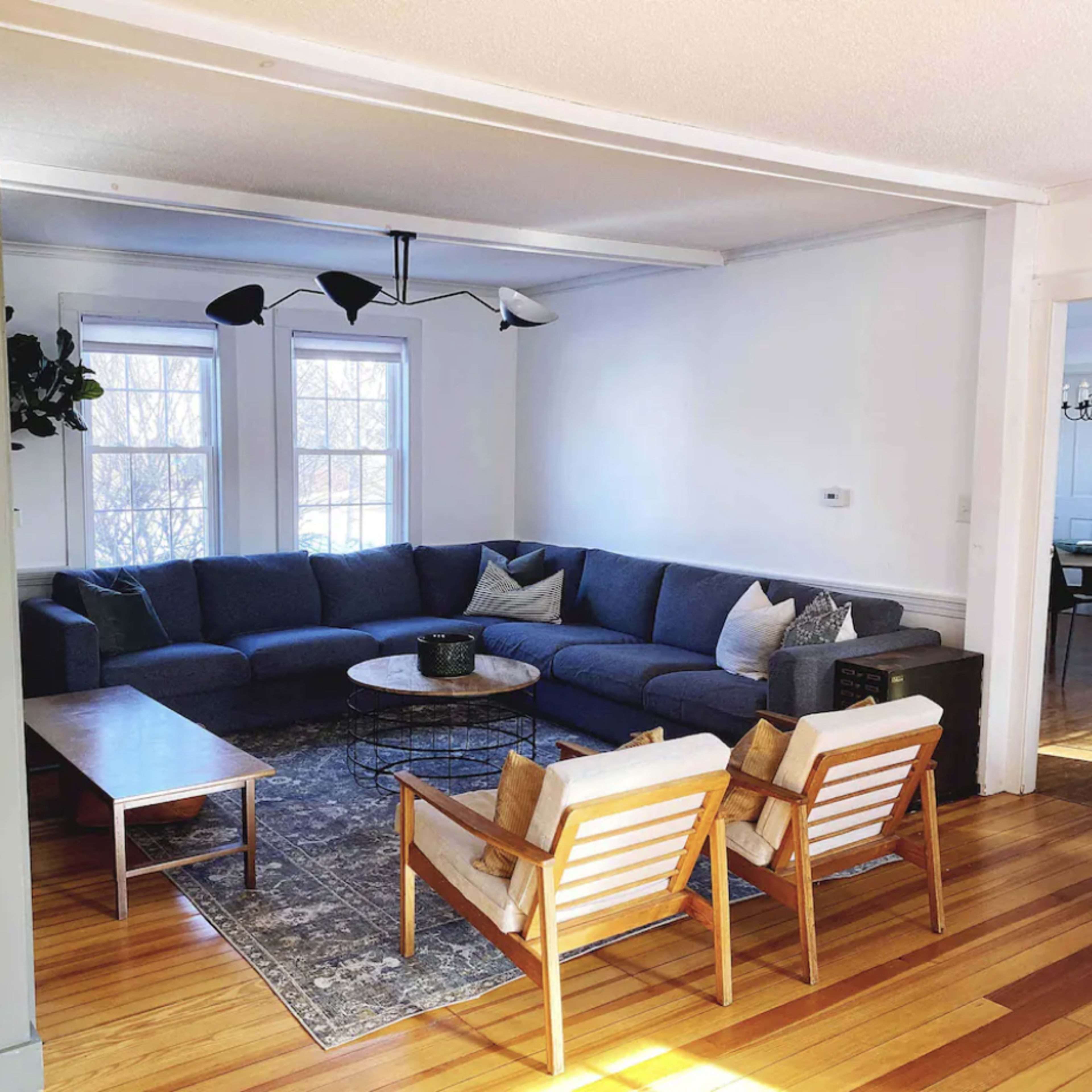 A spacious living room with a large sectional sofa, a round coffee table, and two wooden armchairs arranged on a patterned rug.