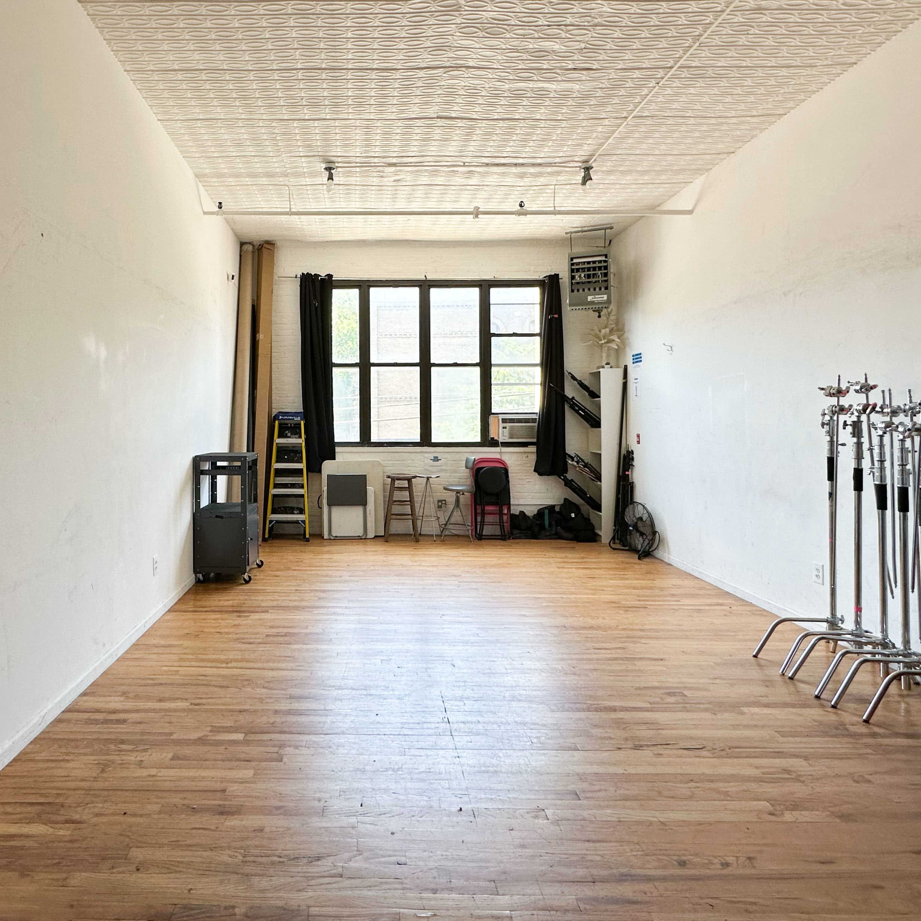 An empty interior space with wooden flooring, large windows, and minimal furnishings along the walls.
