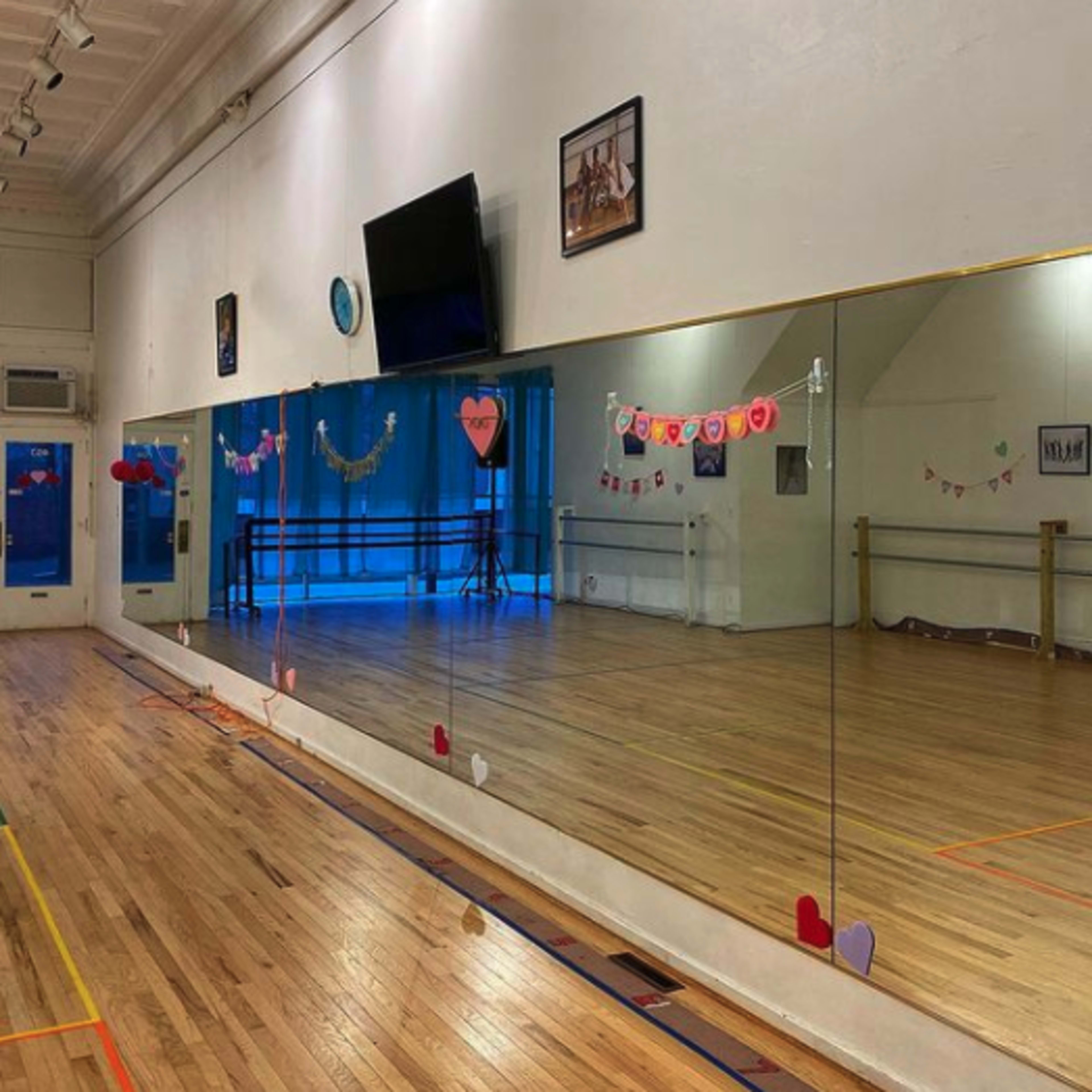 A dance studio with wooden flooring, large mirrors along one wall, and decorations including hearts and banners.