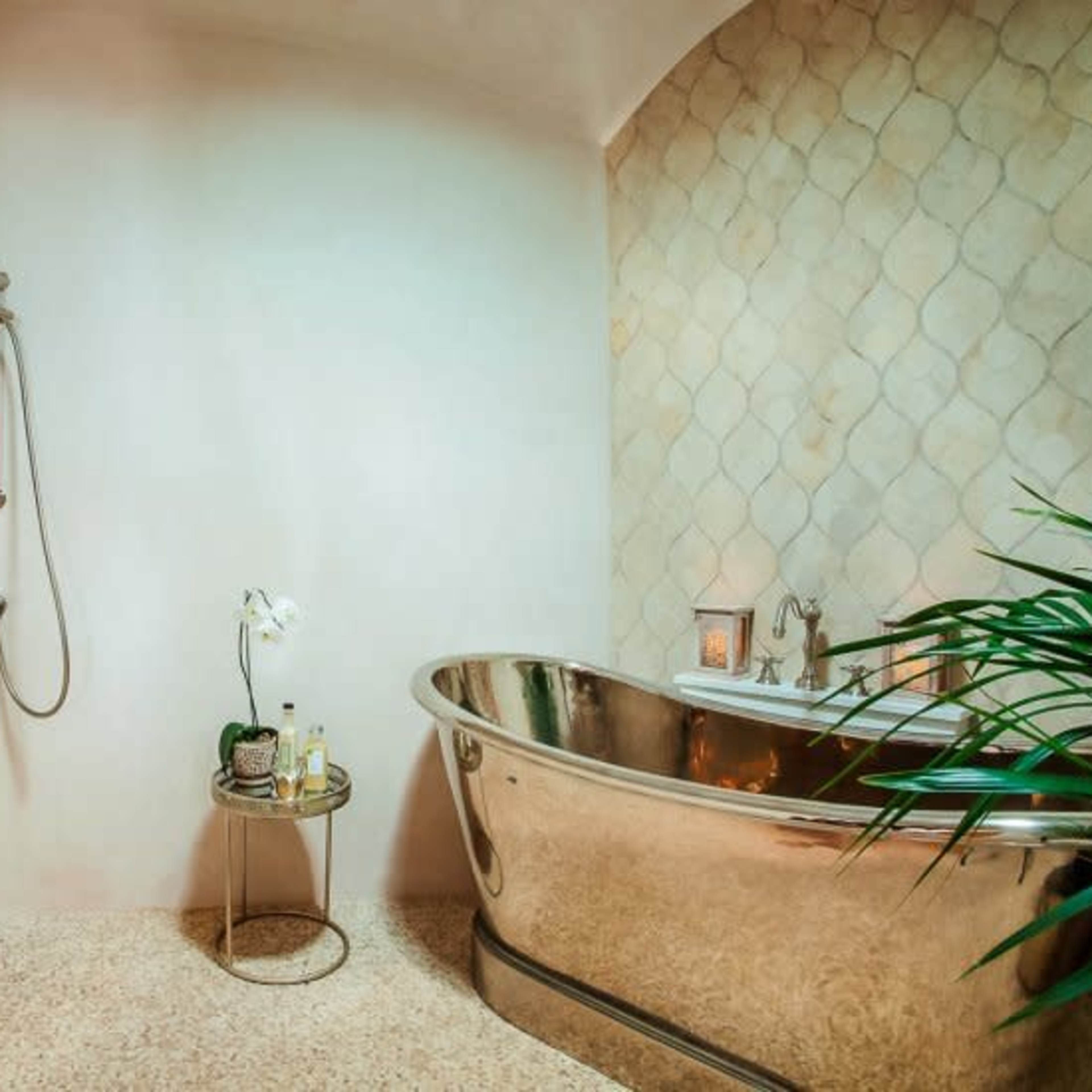 A modern bathroom featuring a spacious shower area and a metallic bathtub with a small side table holding toiletries and a decorative plant.