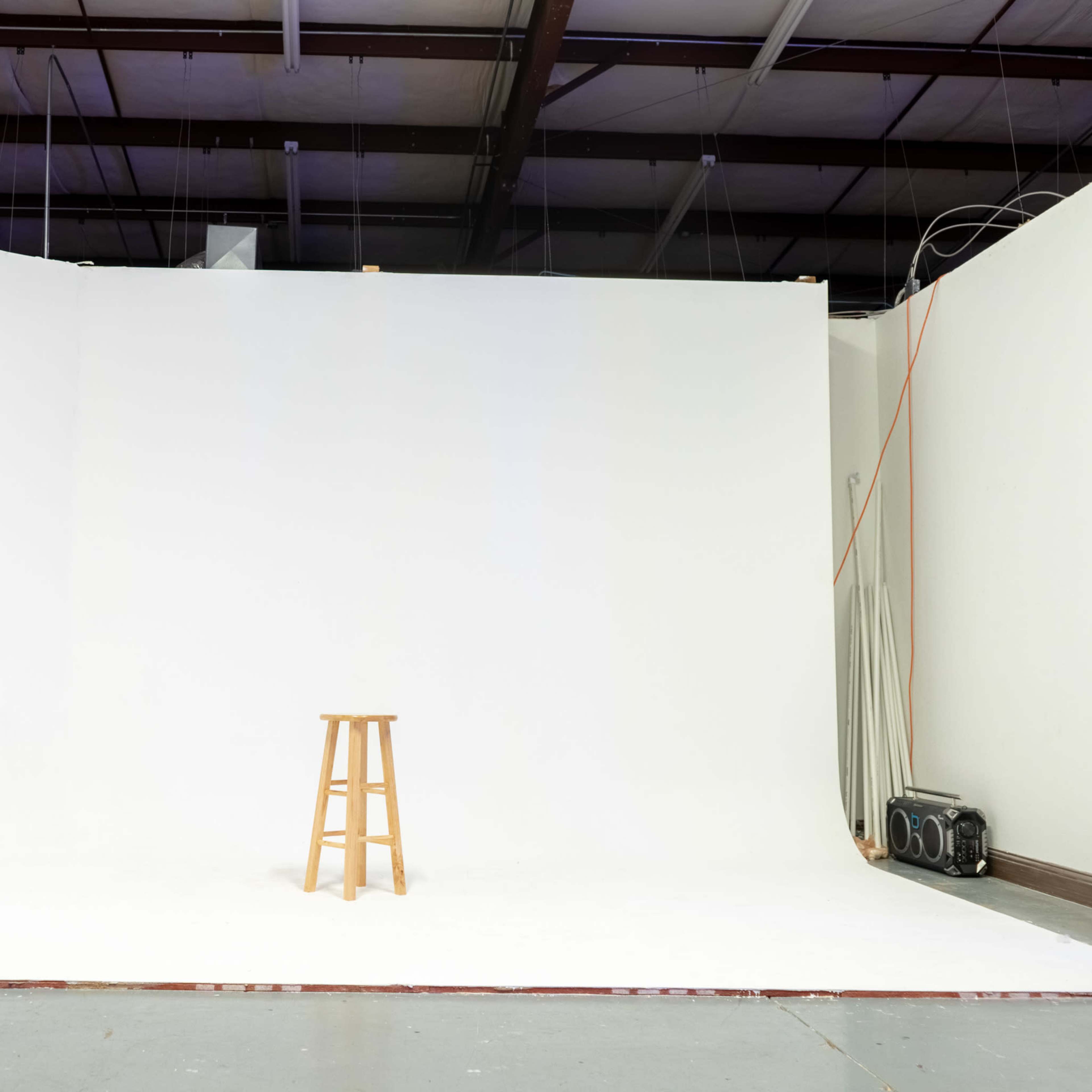 A simple photo studio features a white backdrop and a wooden stool positioned in the center.
