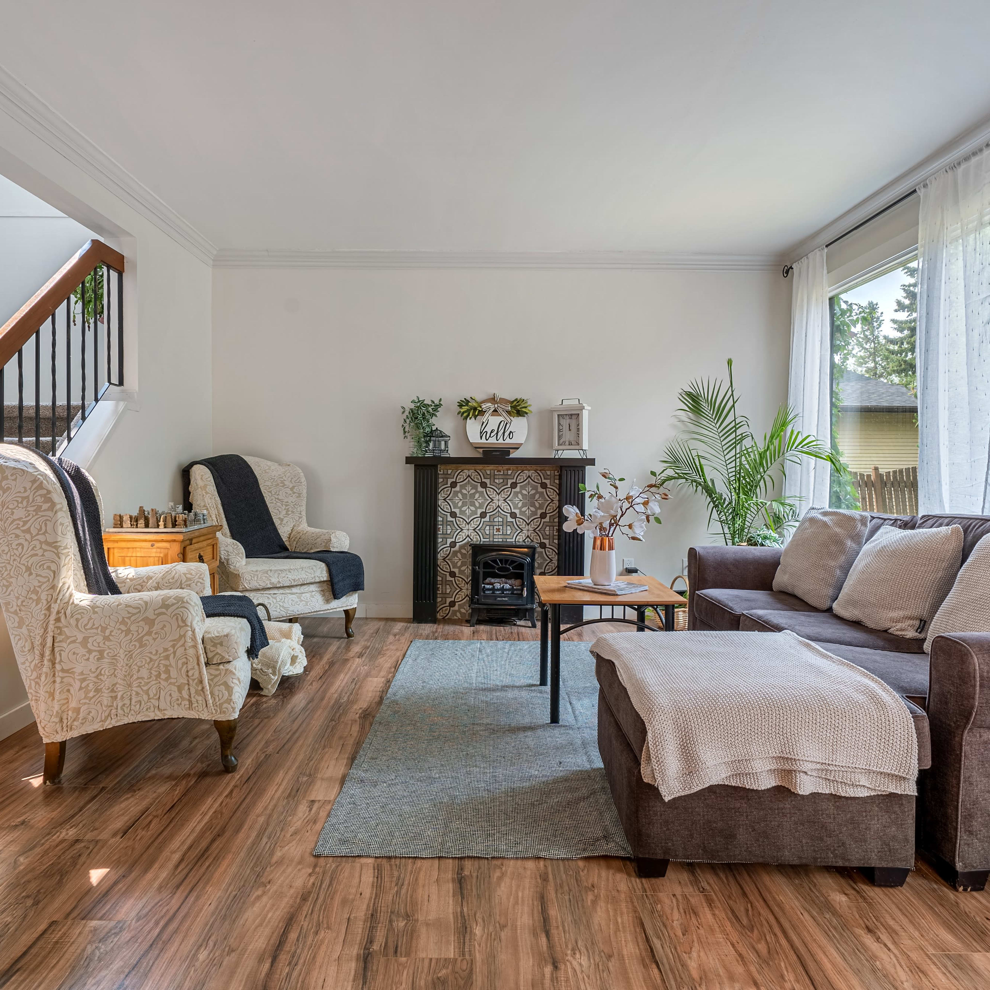 A living room with a staircase, featuring two armchairs, a brown sofa, a coffee table, and a decorative fireplace.