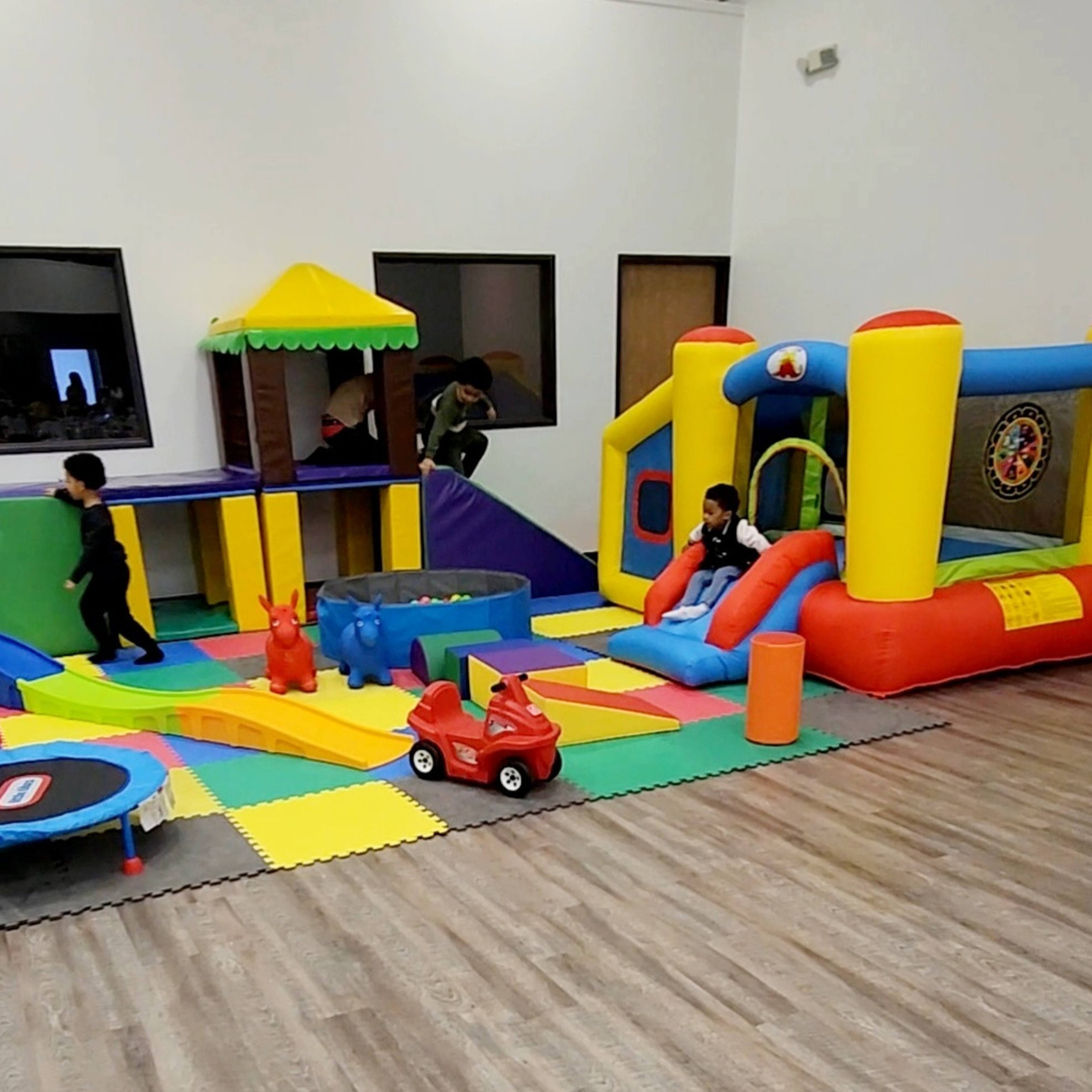 A colorful indoor play area featuring inflatable structures, a trampoline, and various play equipment for children.