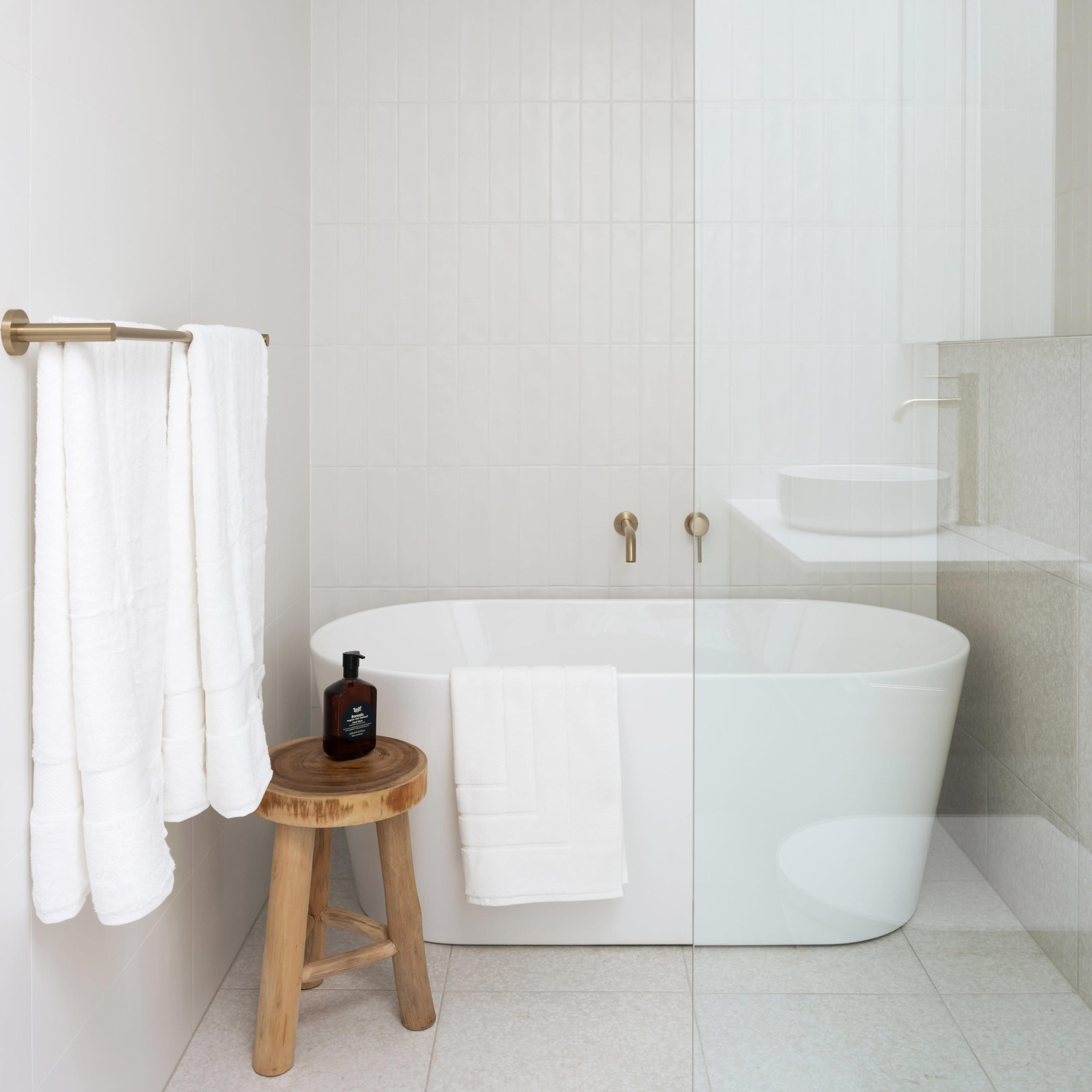A modern bathroom features a freestanding tub, a wooden stool, and neatly arranged white towels.