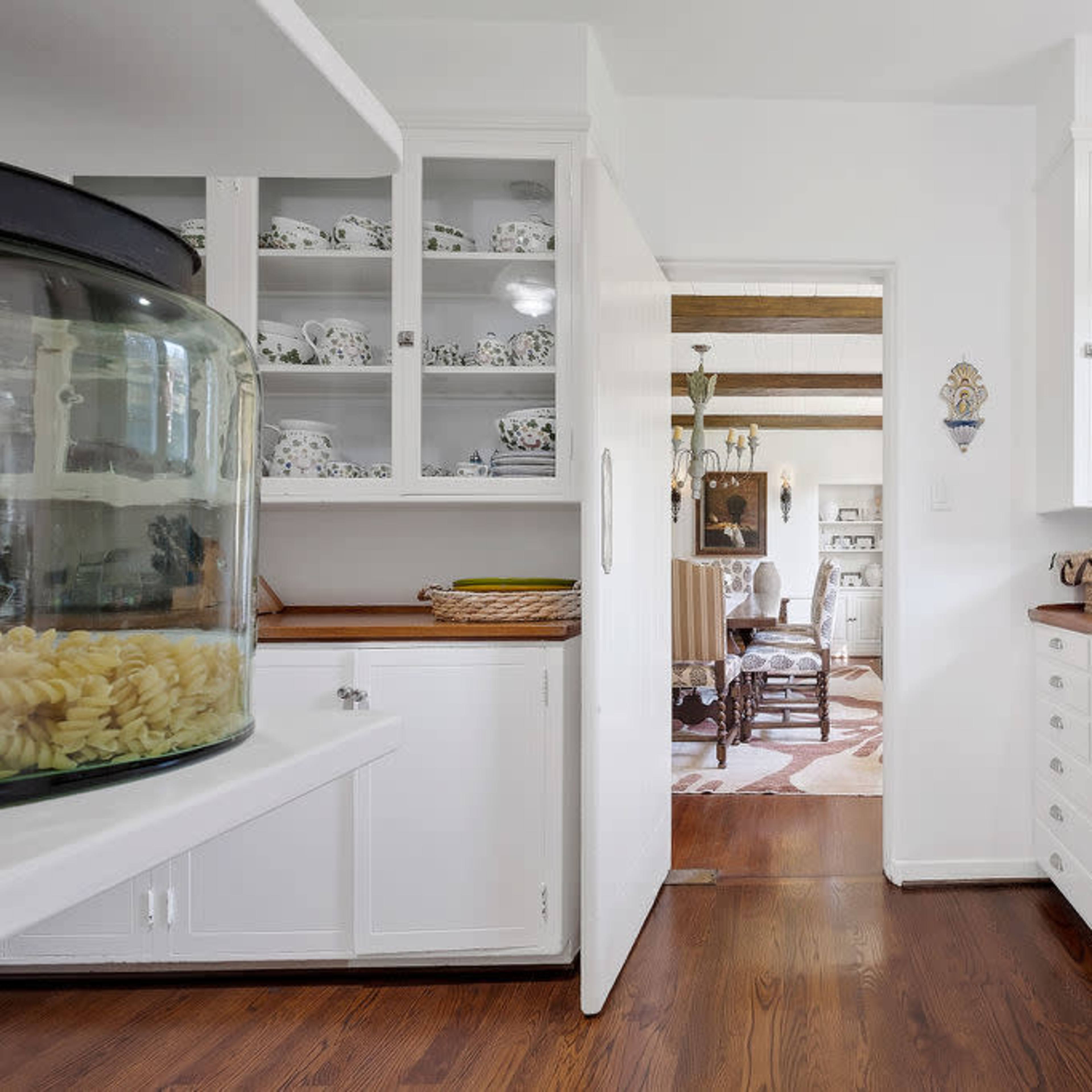 A bright, modern kitchen with white cabinets, wooden countertops, and a view into an adjoining room.