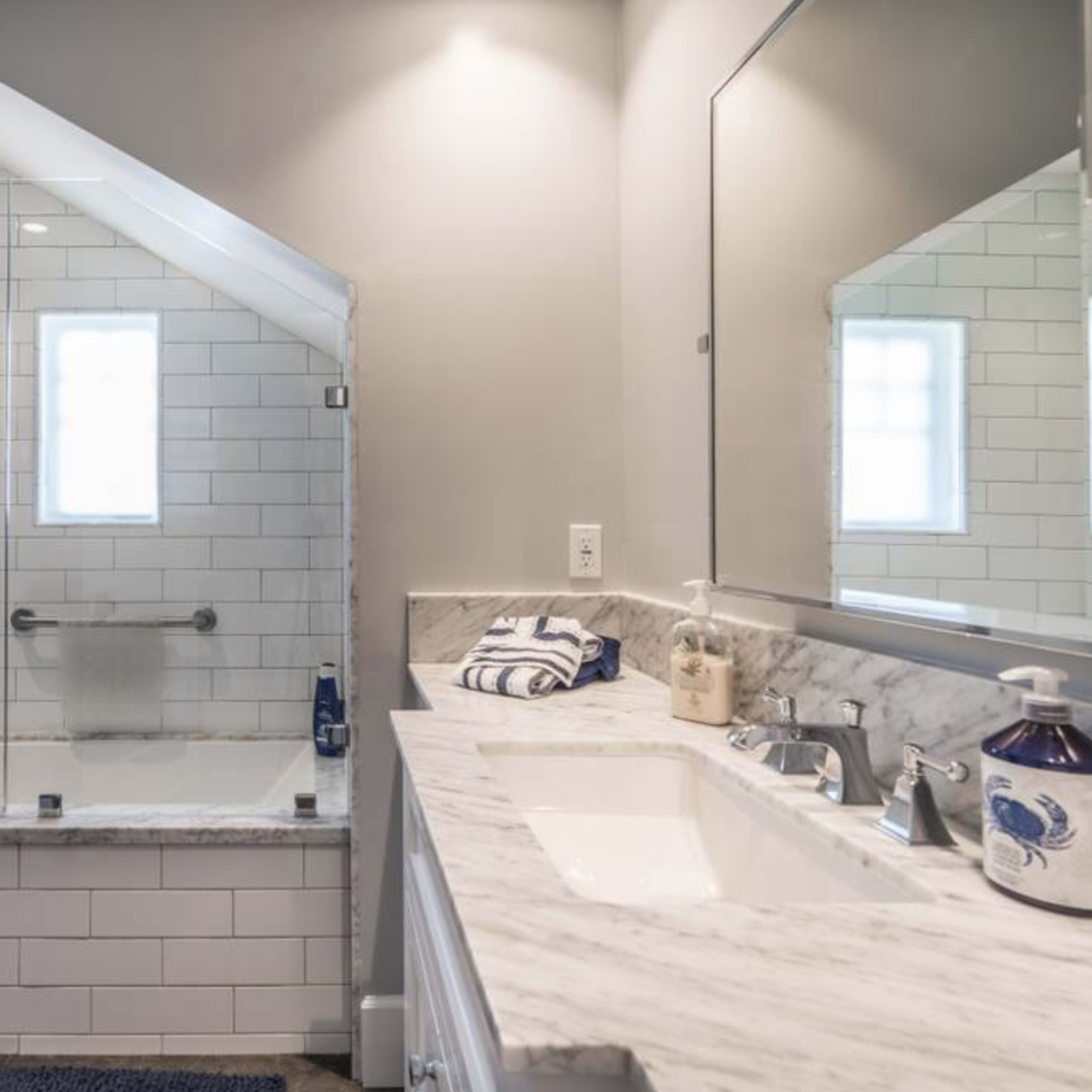 A modern bathroom with a glass-enclosed shower, a white bathtub, and a marble countertop with two sinks.