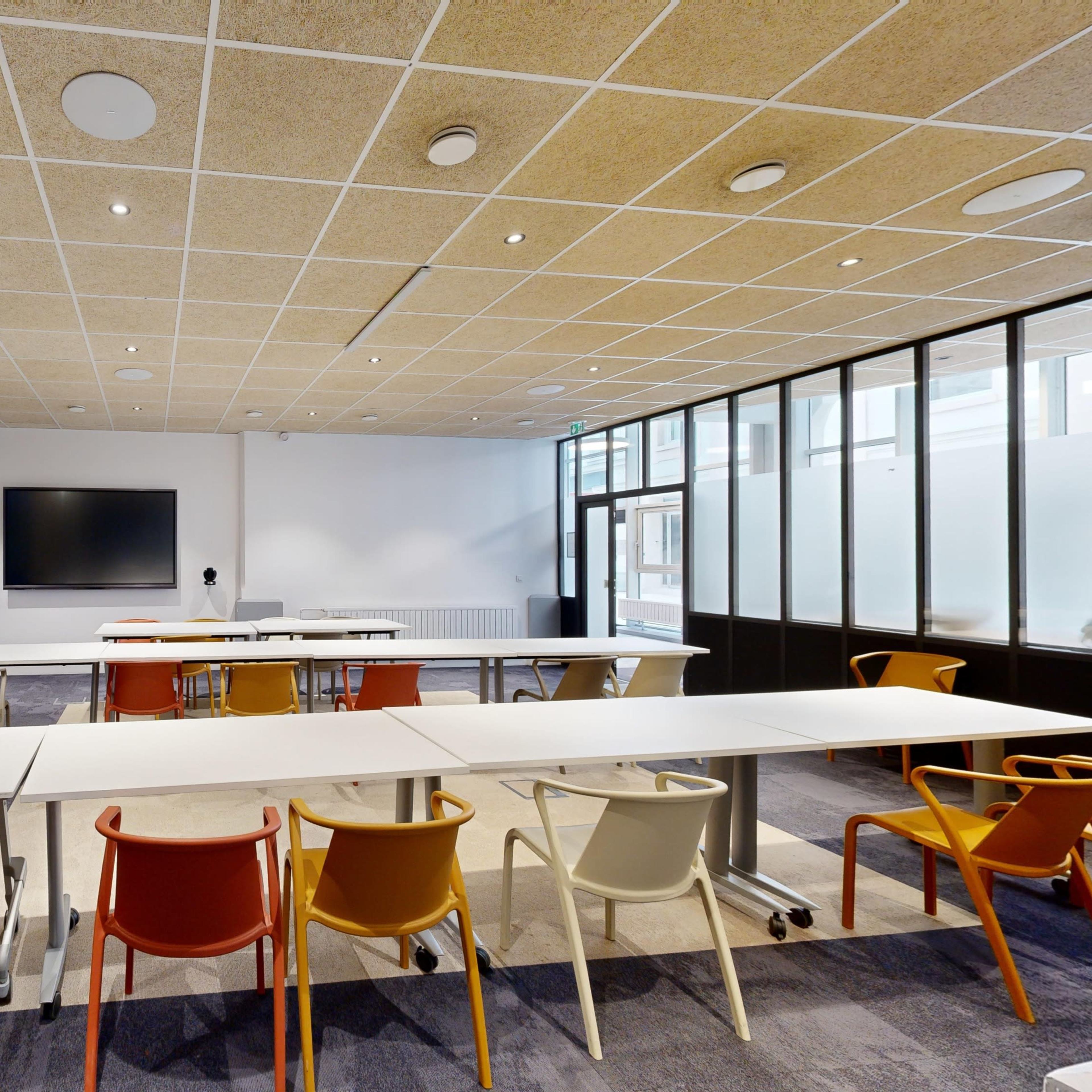 A modern conference room features multiple tables, colorful chairs, and large screens for presentations.