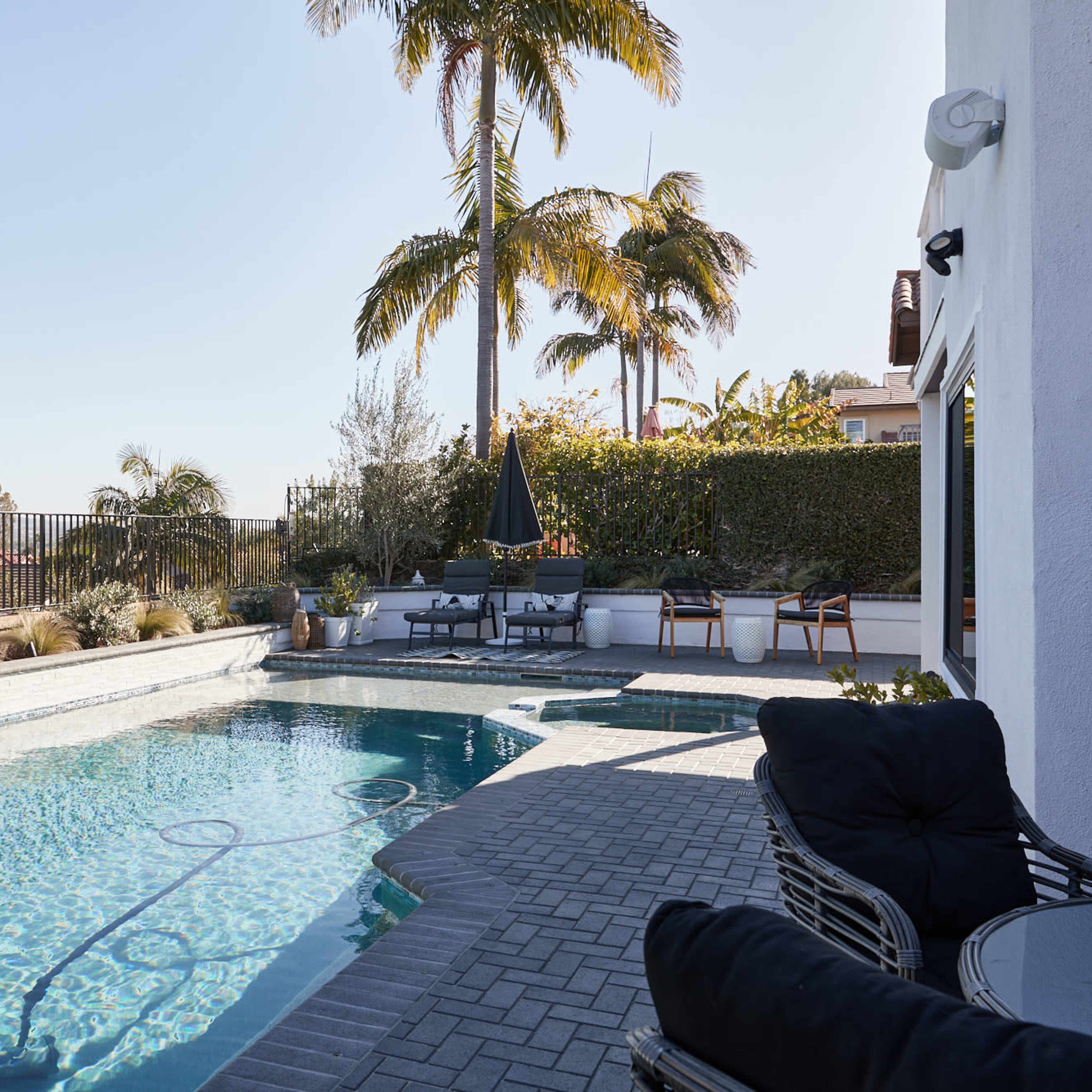 A pool area features a blue swimming pool surrounded by palm trees and seating arrangements under a clear sky.