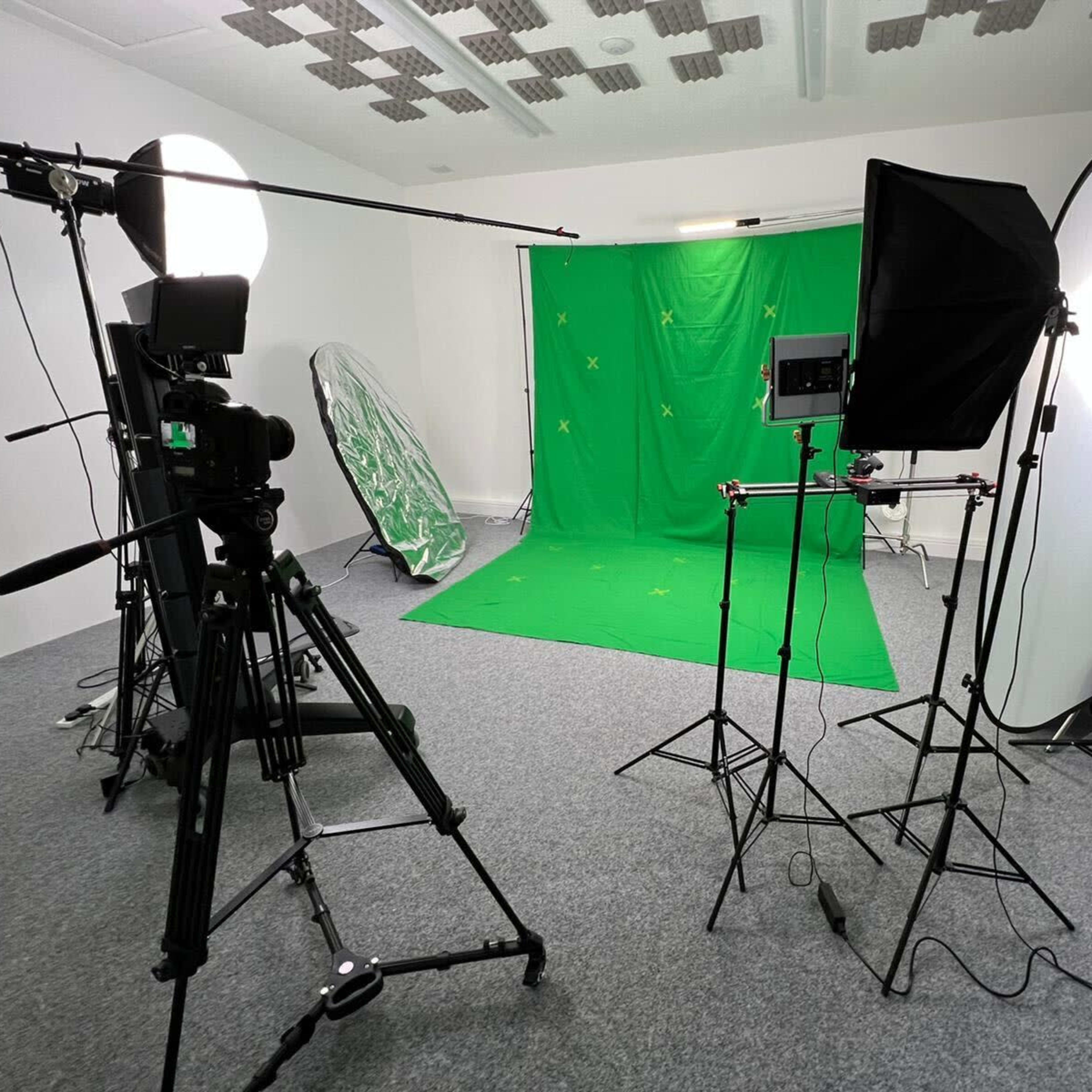 A photography studio set up with a green backdrop, tripods, and lighting equipment arranged for a video or photo shoot.