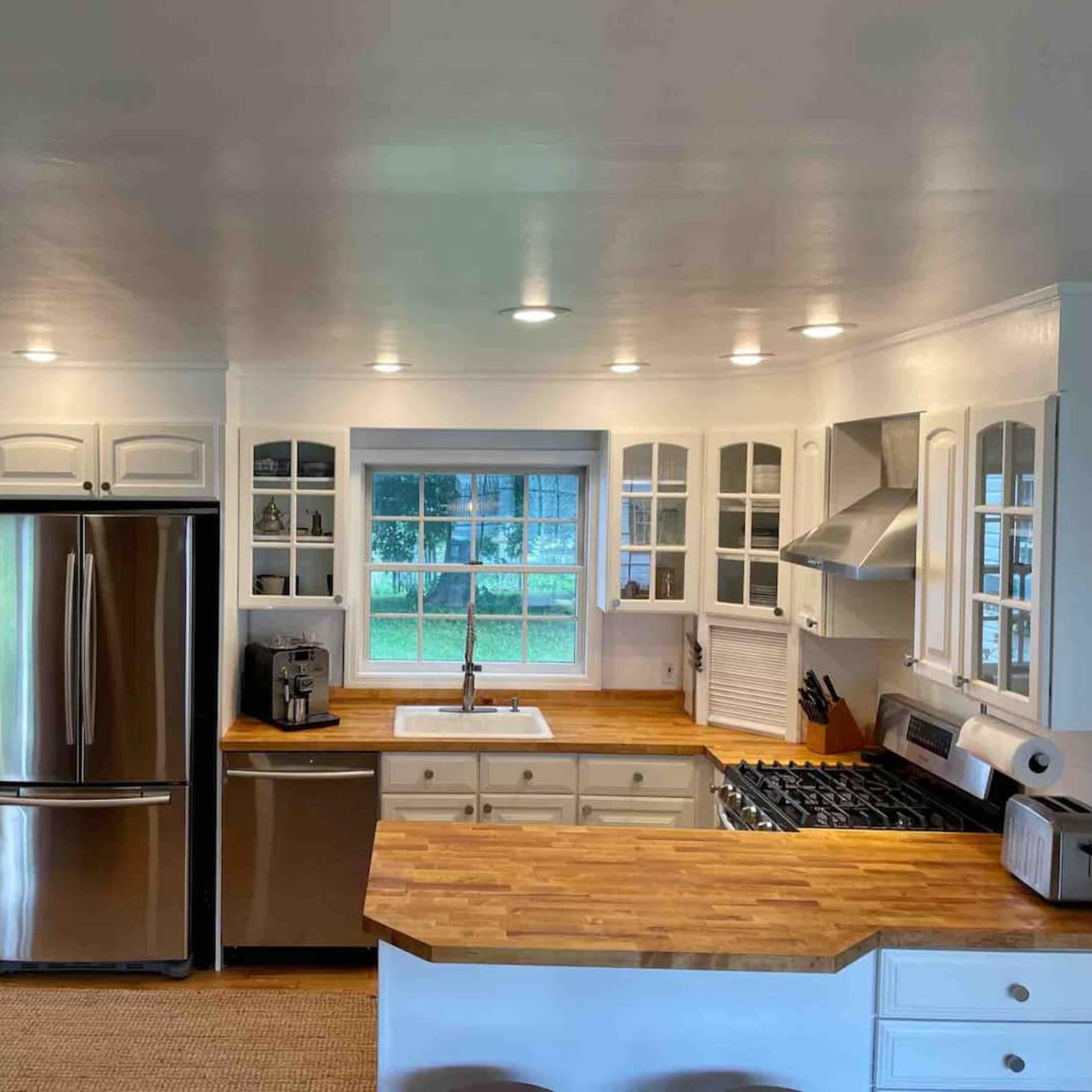 A modern kitchen features white cabinetry, a stainless steel refrigerator, and a central island with a wooden countertop.