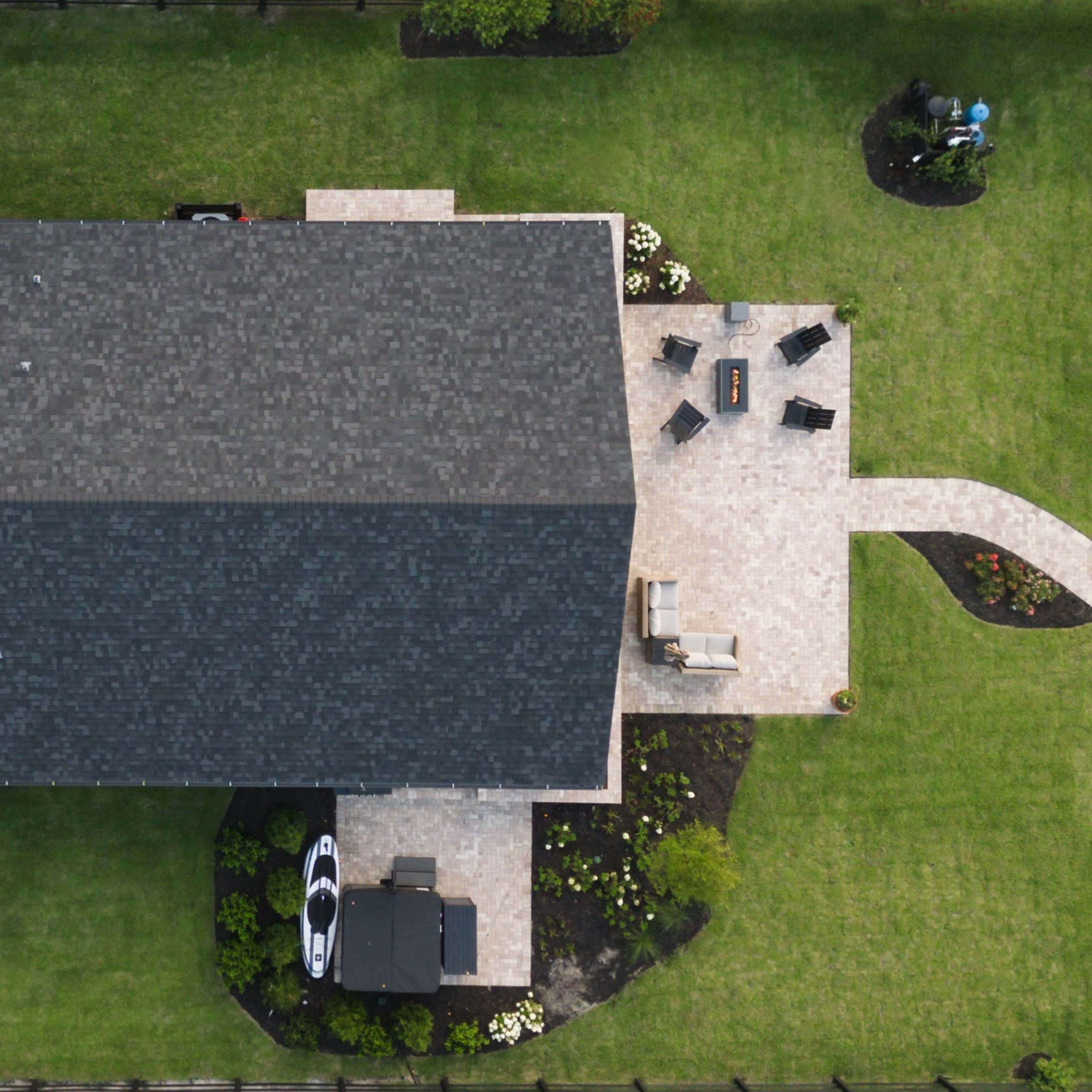 An aerial view of a house surrounded by a well-manicured lawn and a stone pathway leading to a patio with seating.