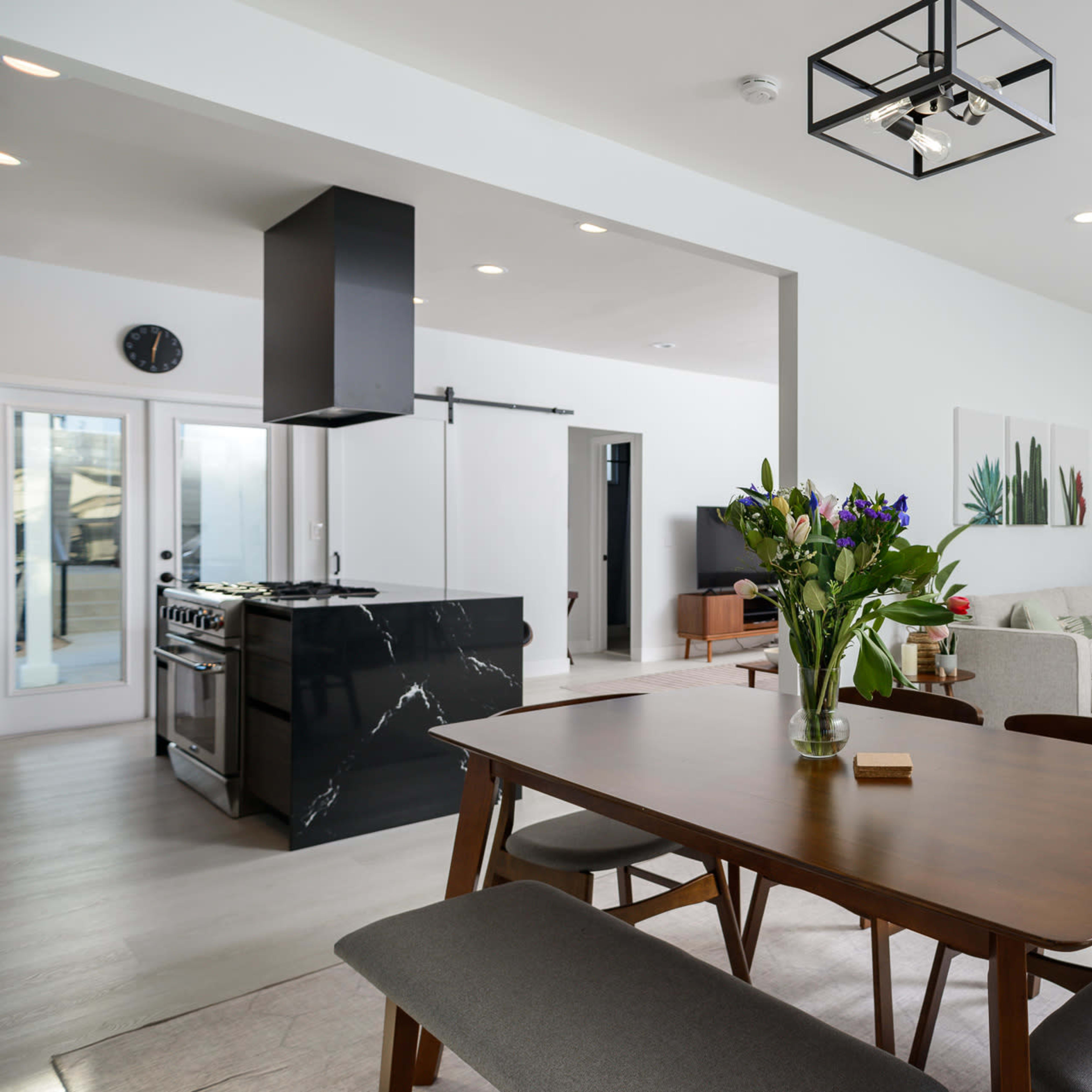 A modern open-concept living and dining area features a wooden dining table, a sleek kitchen island, and a comfortable seating space with plants and artwork.