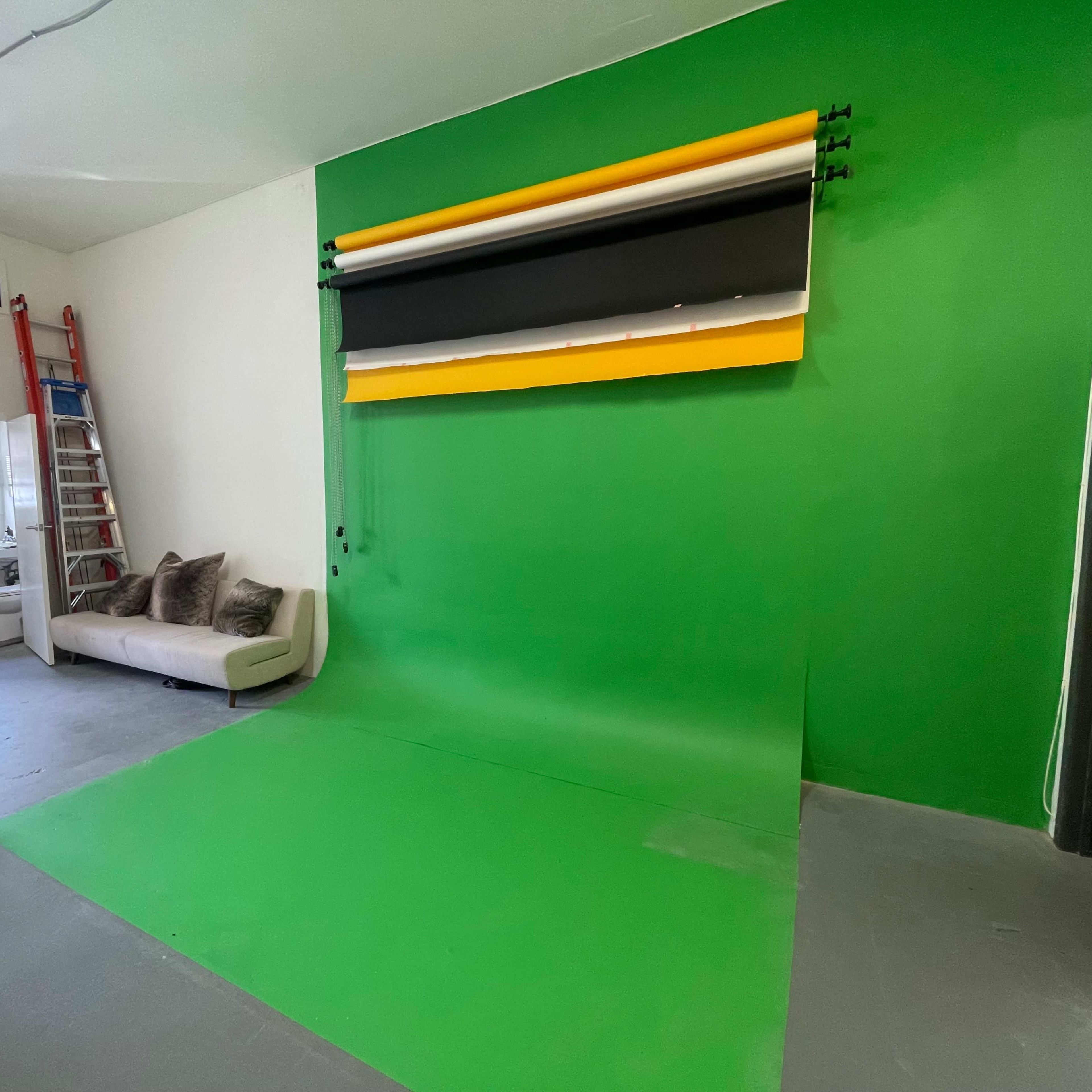A studio space with a green backdrop, a white wall, a sofa, and a ladder leaning against the wall.