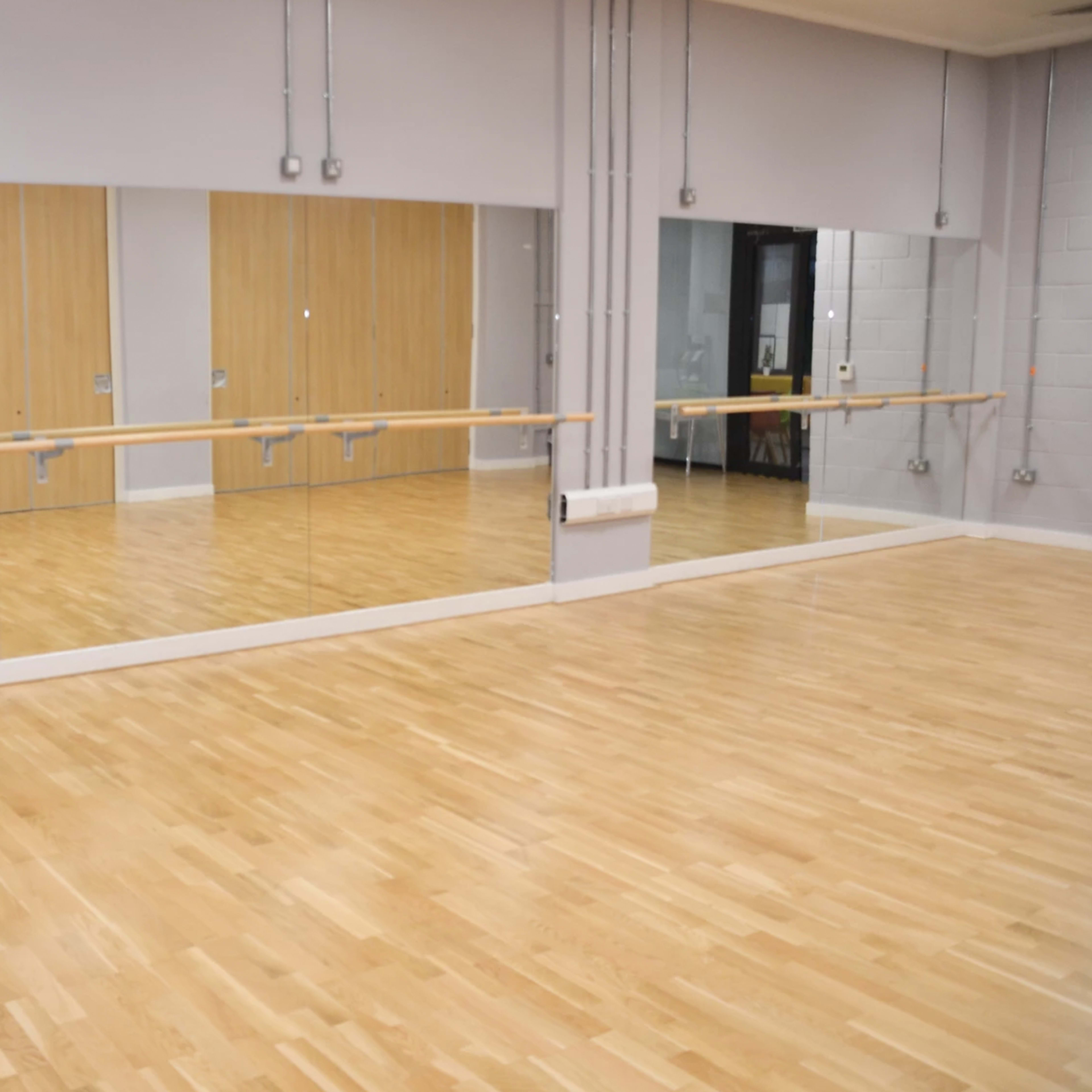 An empty dance studio with wooden floors and large mirrors on one wall.