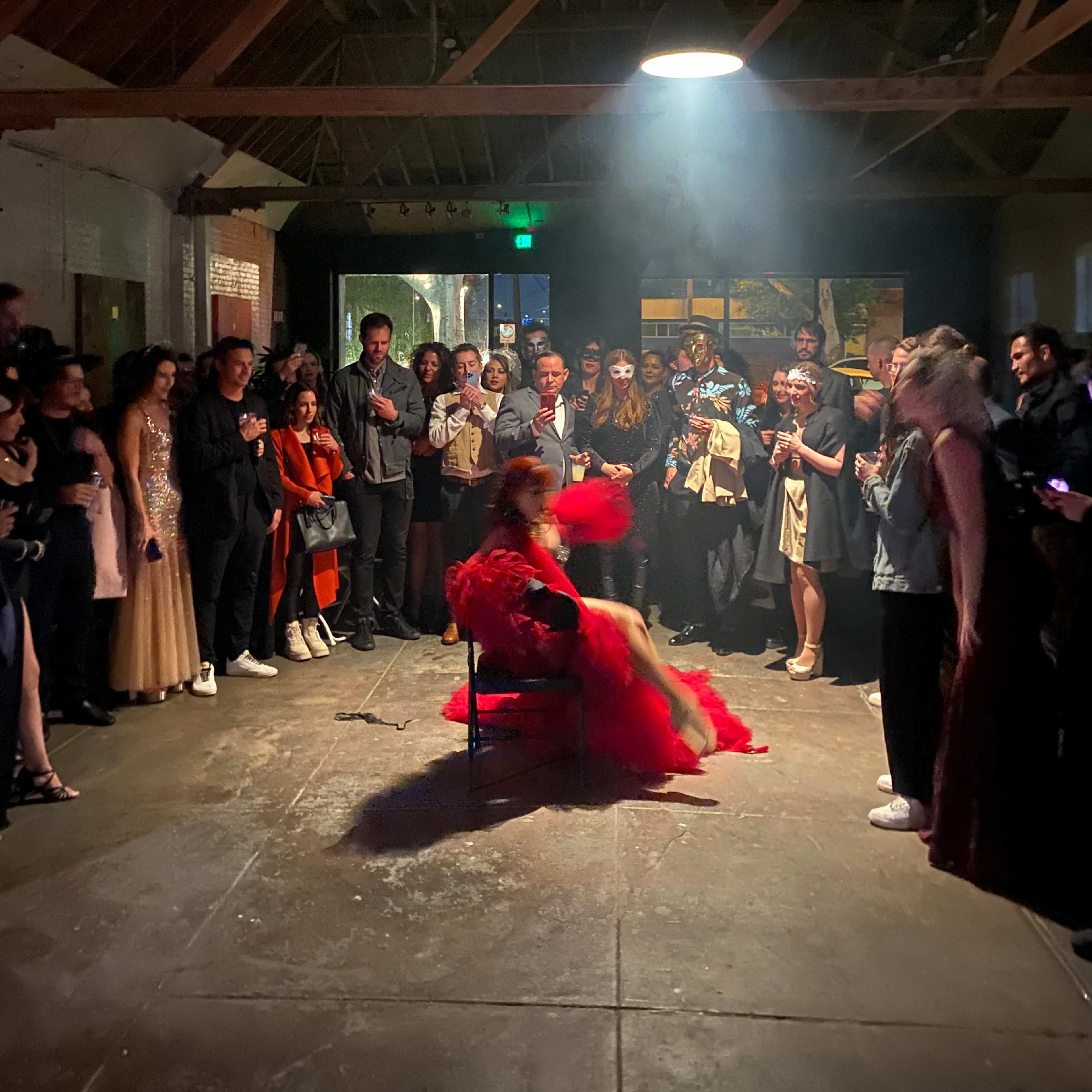 A performer in a red outfit entertains an audience seated in a dimly lit venue with exposed wooden beams.