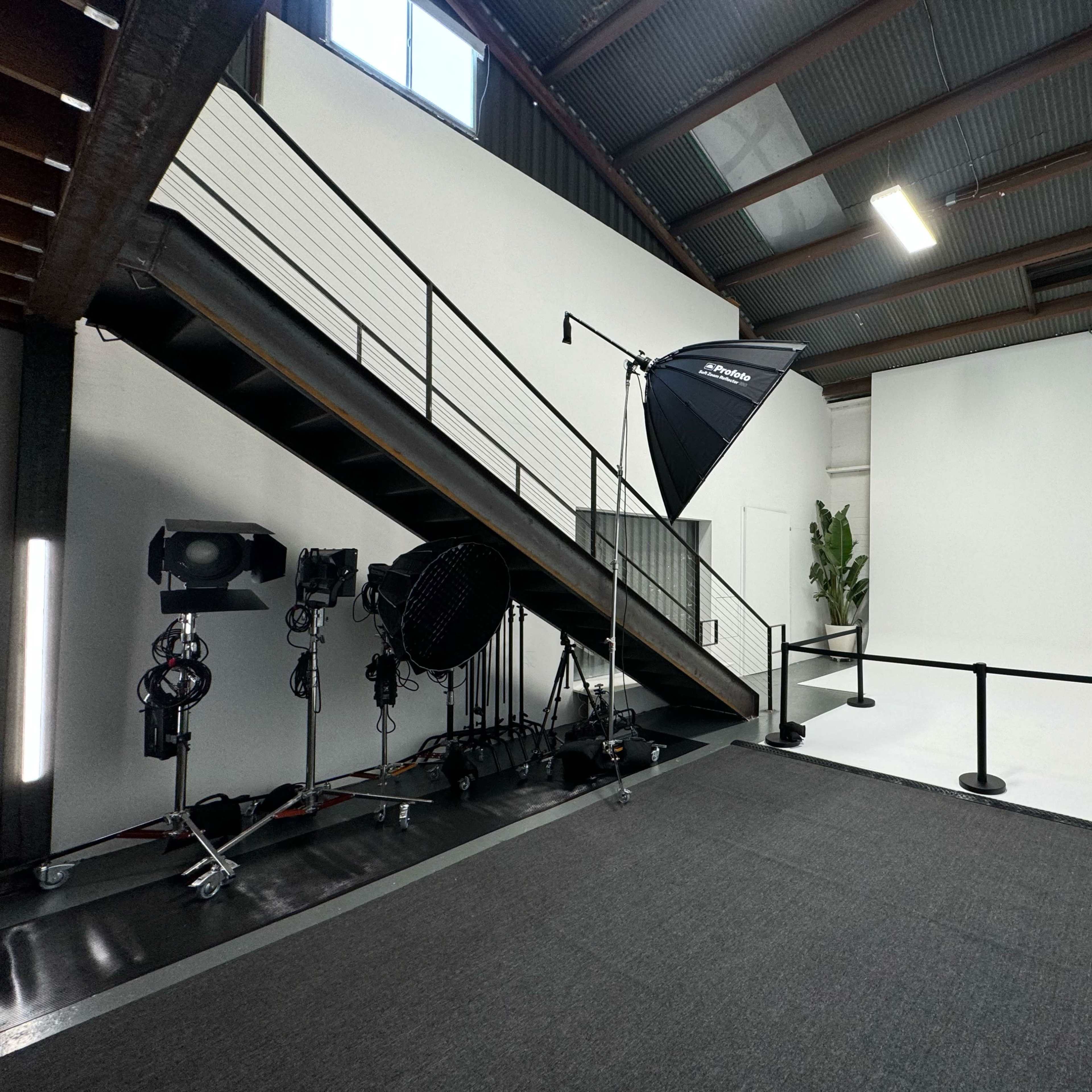 An industrial-style studio with a staircase, lighting equipment, and a plain white backdrop.
