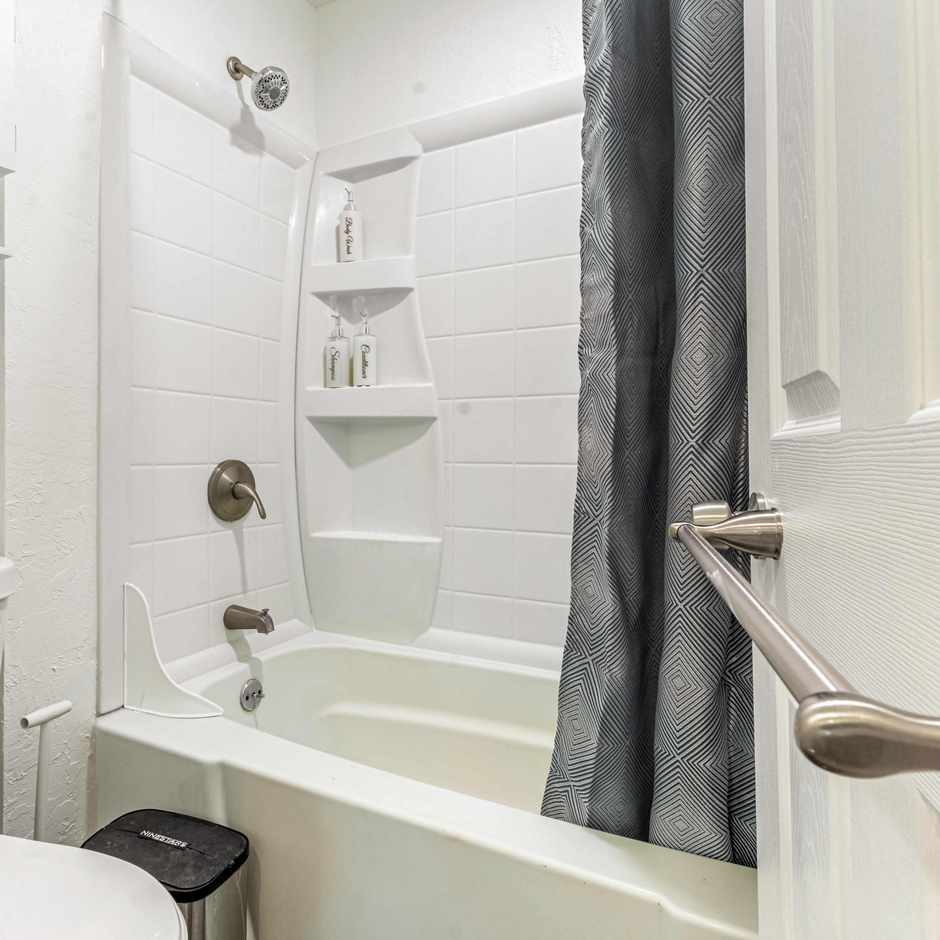 A bathroom featuring a bathtub with a shower, a toilet, and shelves for storage.