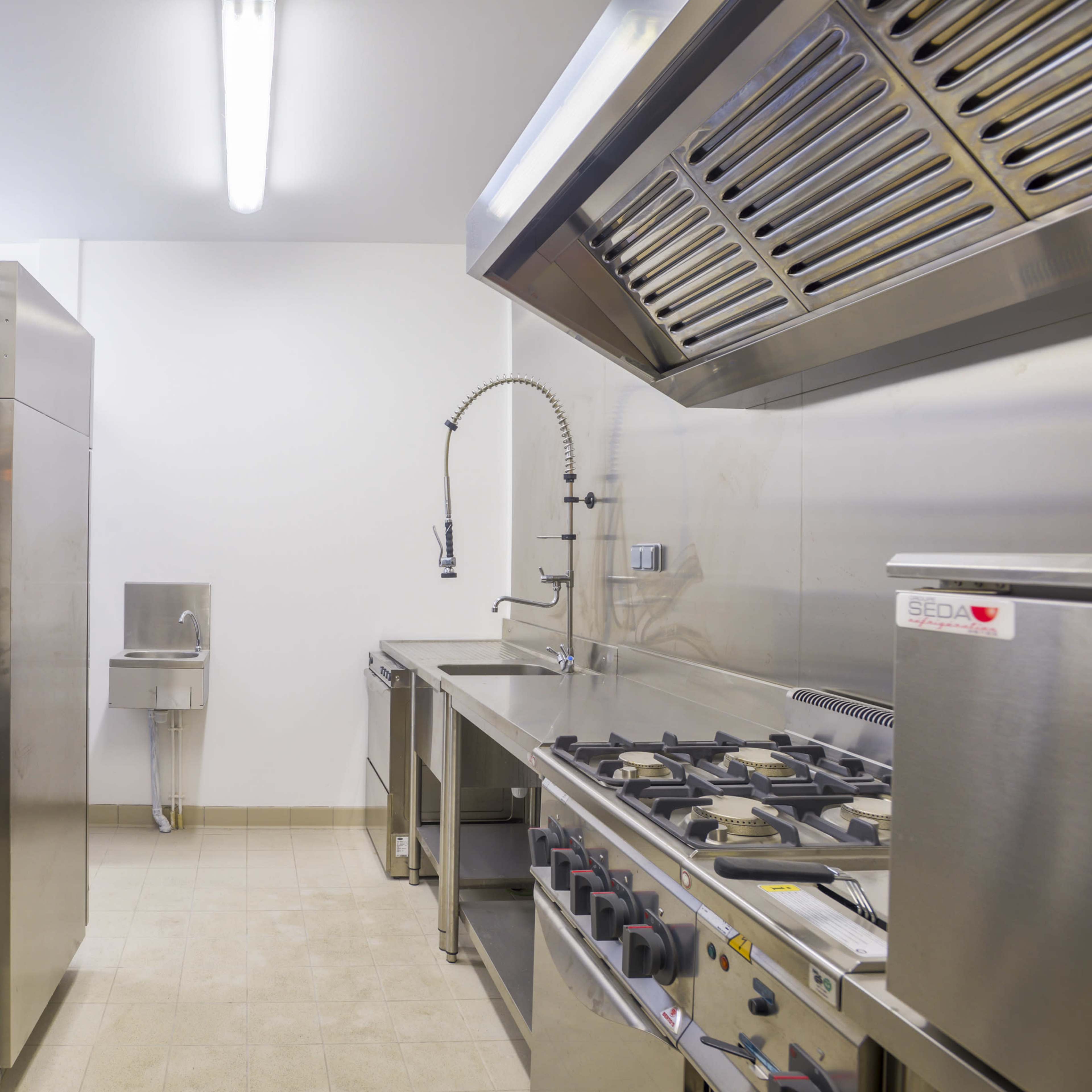 A commercial kitchen with stainless steel appliances, including sinks, a stove, and a refrigerator.