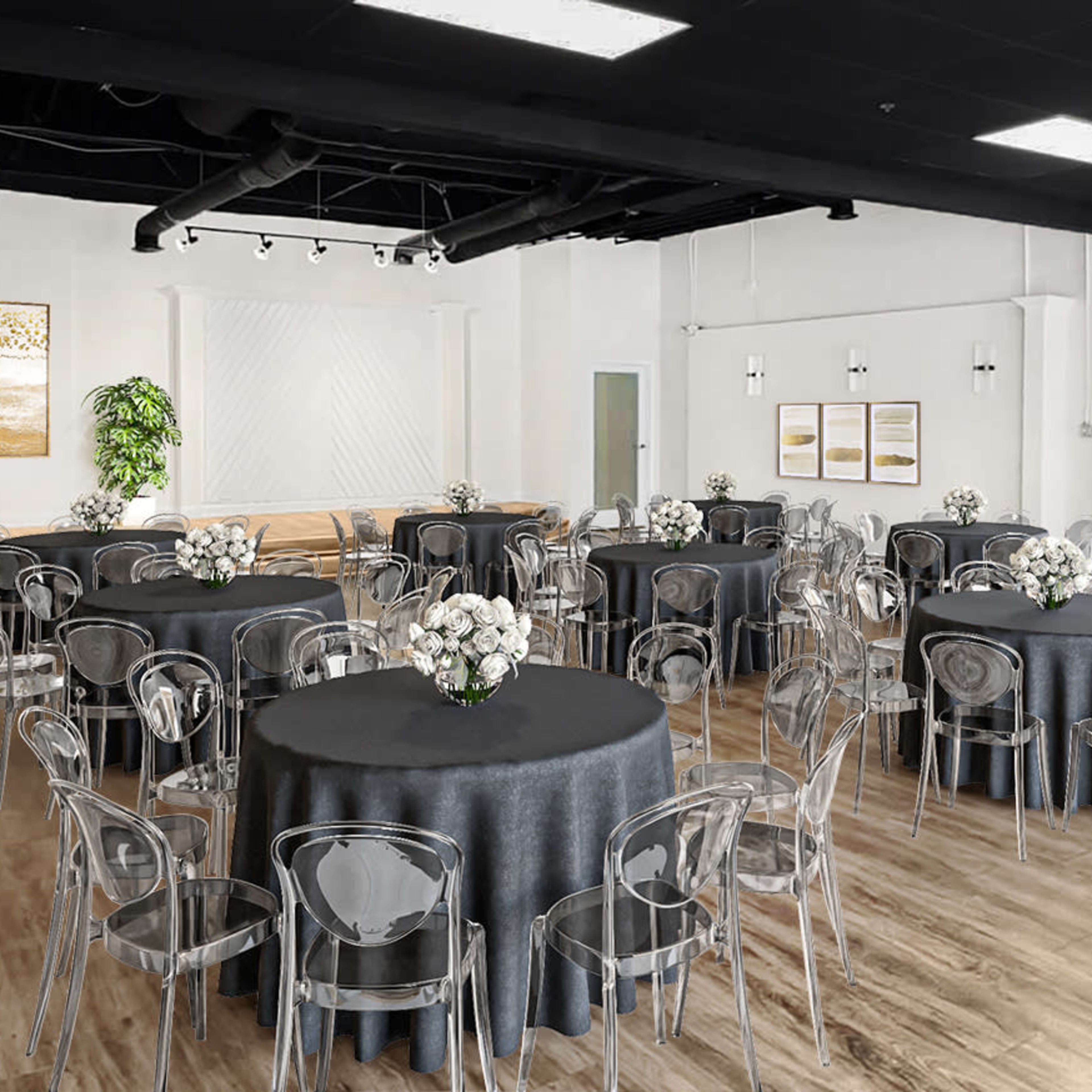 A banquet hall features several round tables covered with dark tablecloths and clear chairs, arranged for an event.