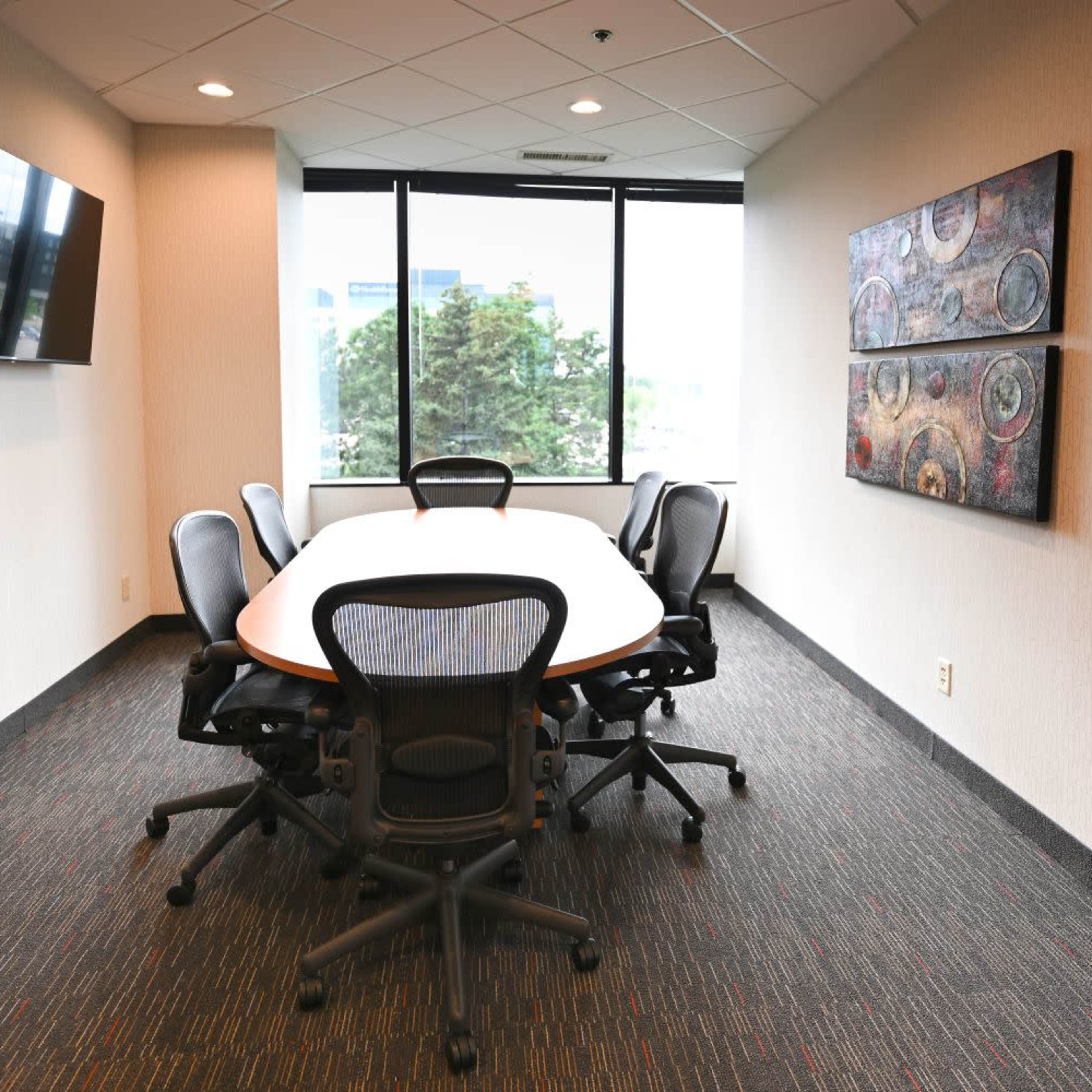A modern conference room with a large oval table surrounded by ergonomic chairs and a wall-mounted television.