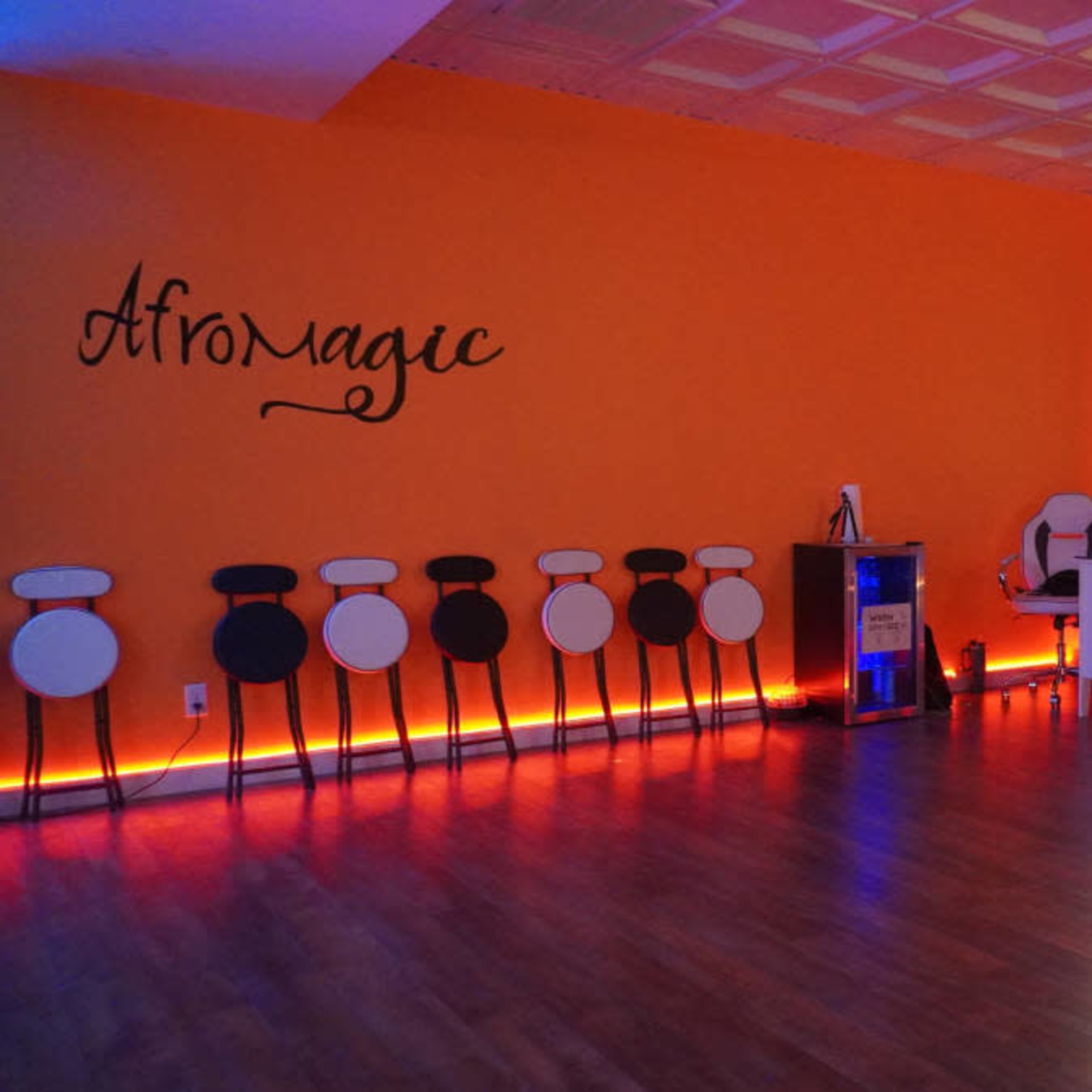The room features an orange wall with "Afromagic" written on it, several black and white stools lined up against the wall, and ambient lighting along the floor.