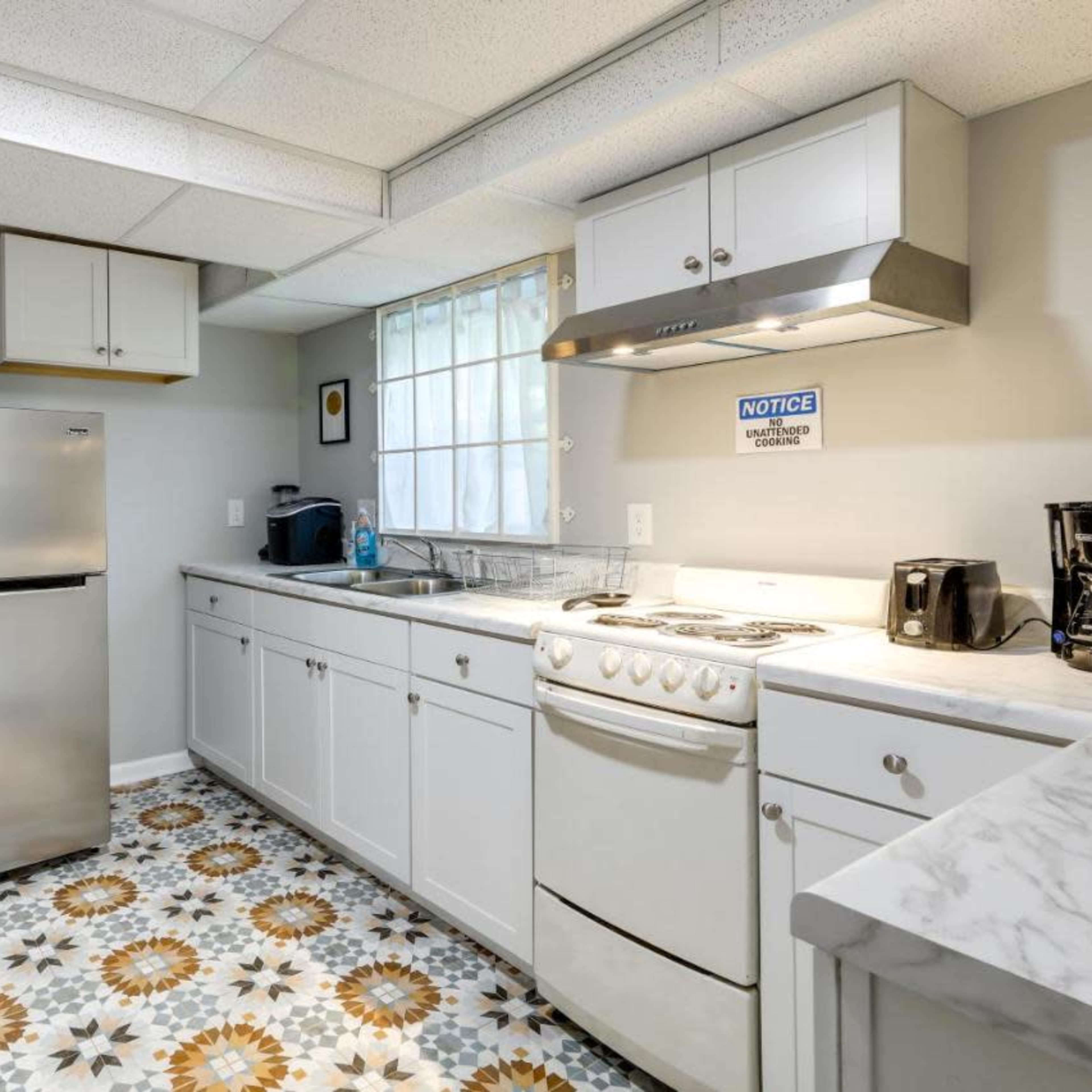 A modern kitchen features a stainless steel refrigerator, white cabinetry, a countertop stove, and patterned flooring.
