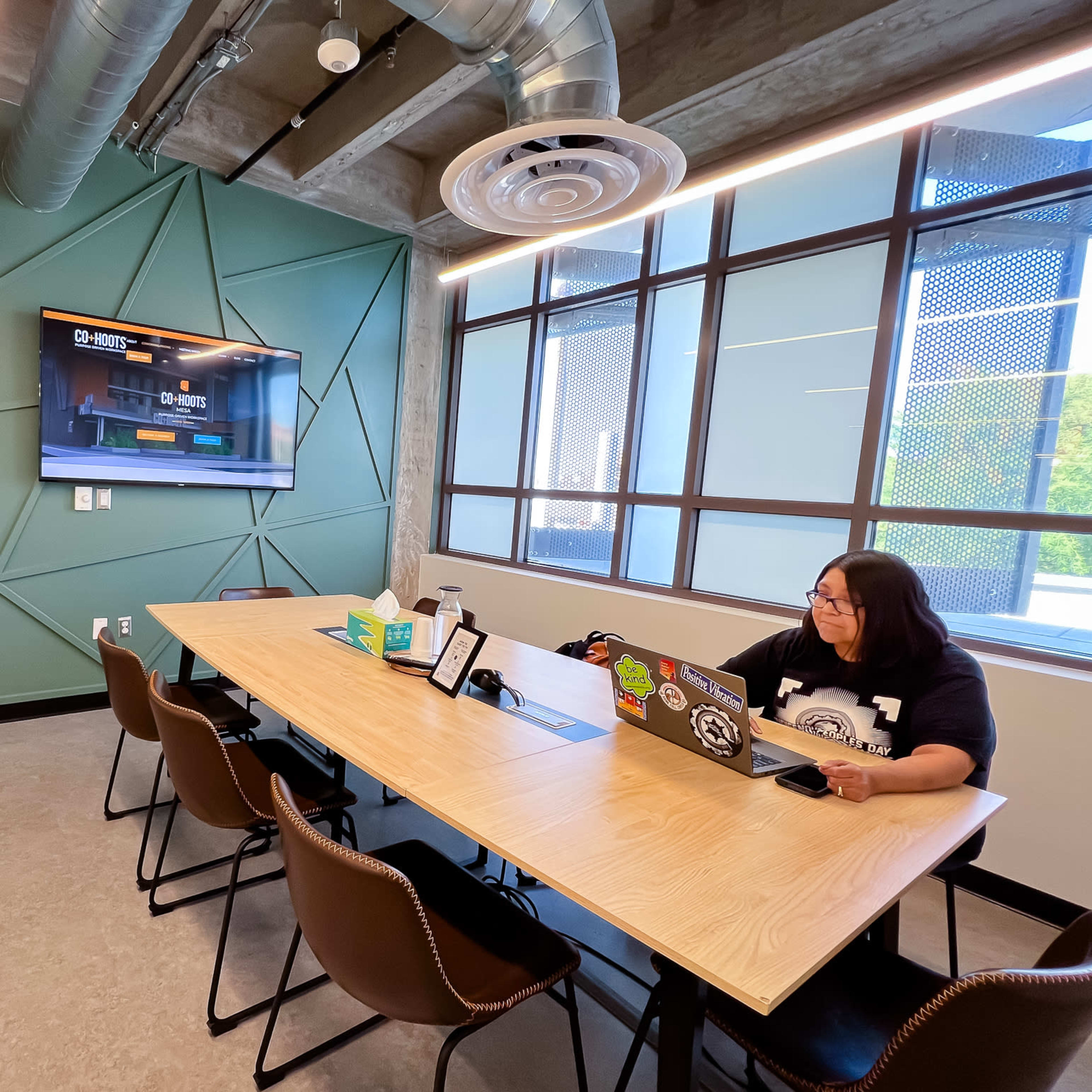 A person sits at a table in a modern conference room with a large wall-mounted screen displaying a gaming interface.