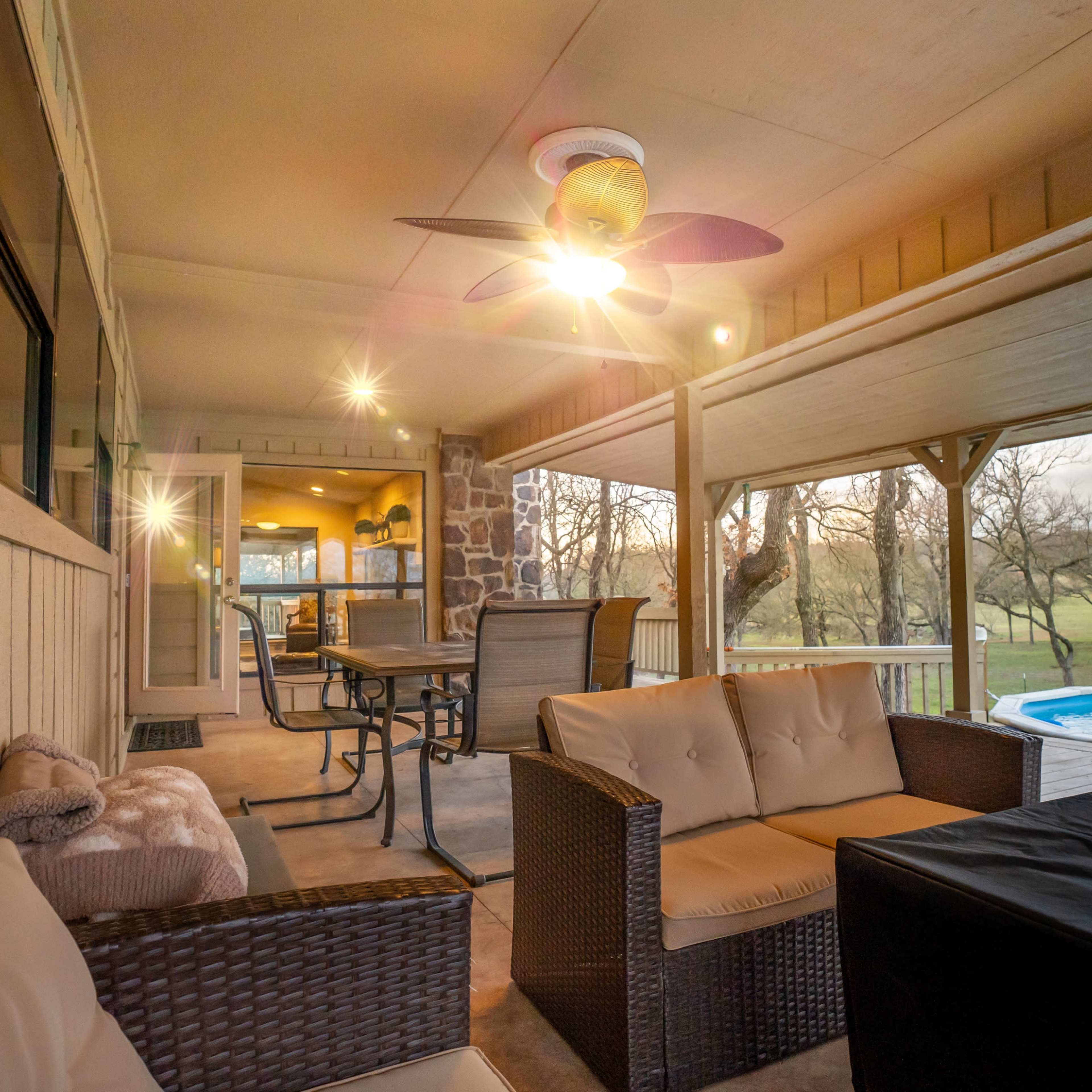 A spacious outdoor patio with seating, a ceiling fan, and a view of a pool and grassy landscape.