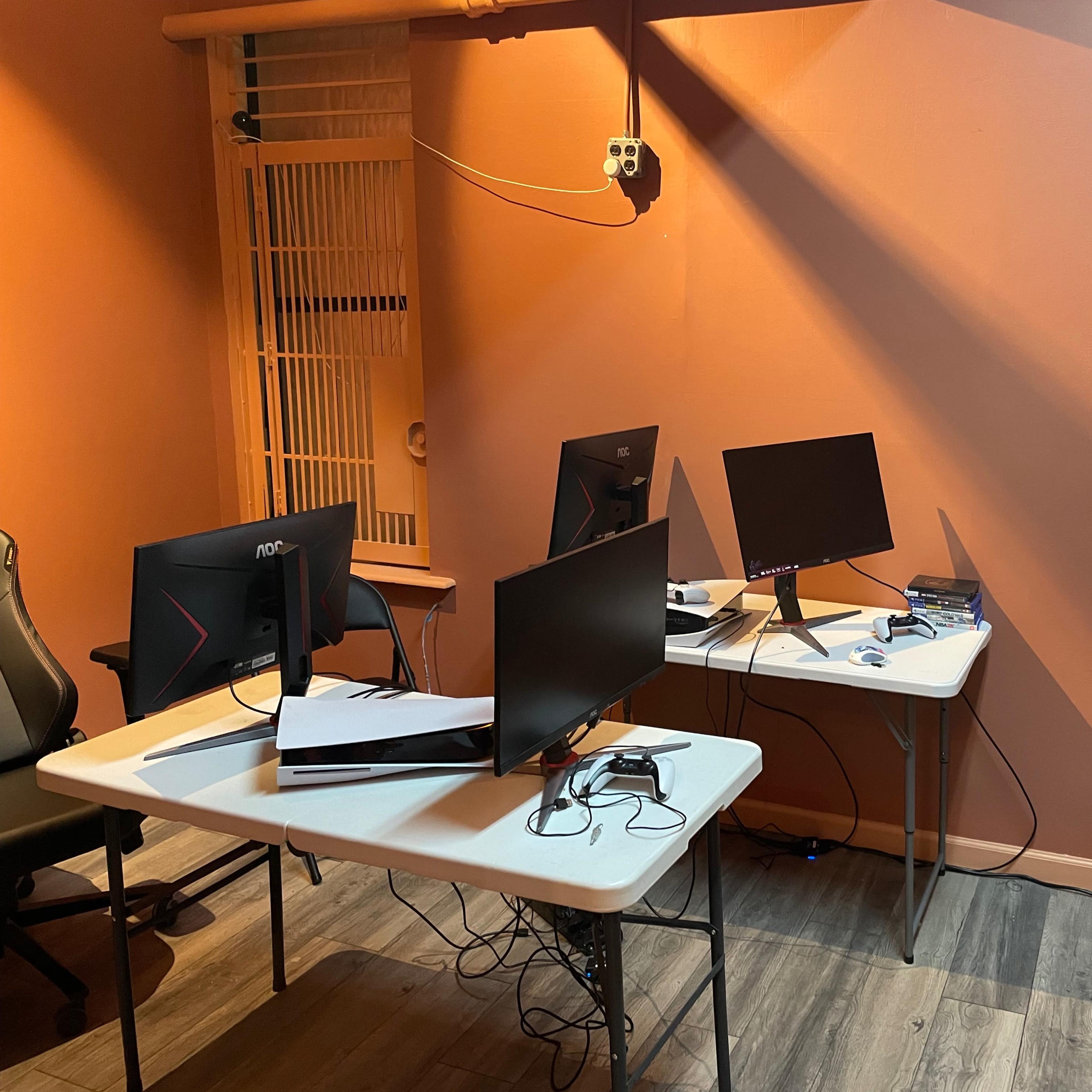 A small room with two tables, each holding a computer monitor, and a chair in the corner, against a backdrop of orange walls.