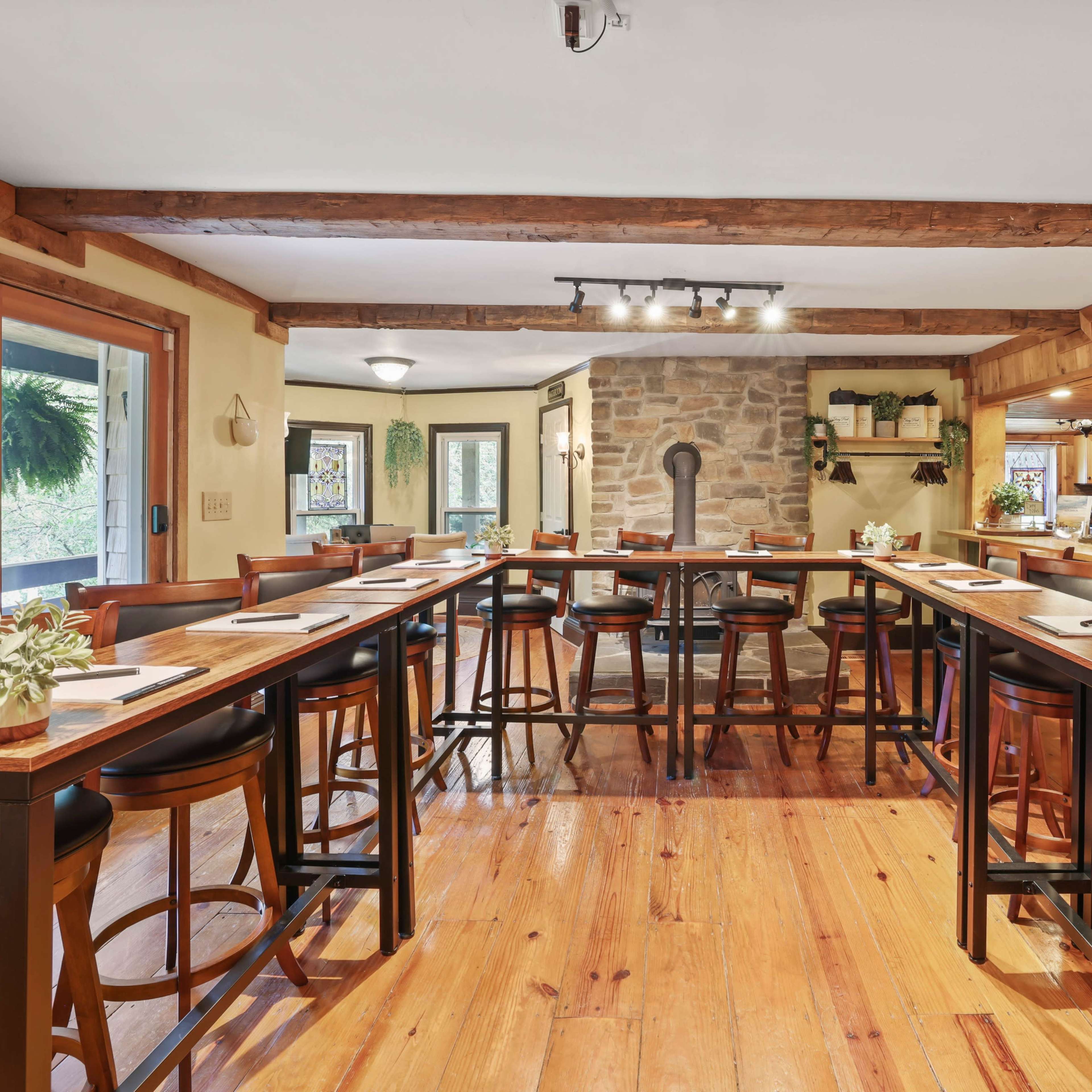 A spacious dining area with a long table and high-backed chairs, illuminated by overhead lights and featuring a stone fireplace in the background.