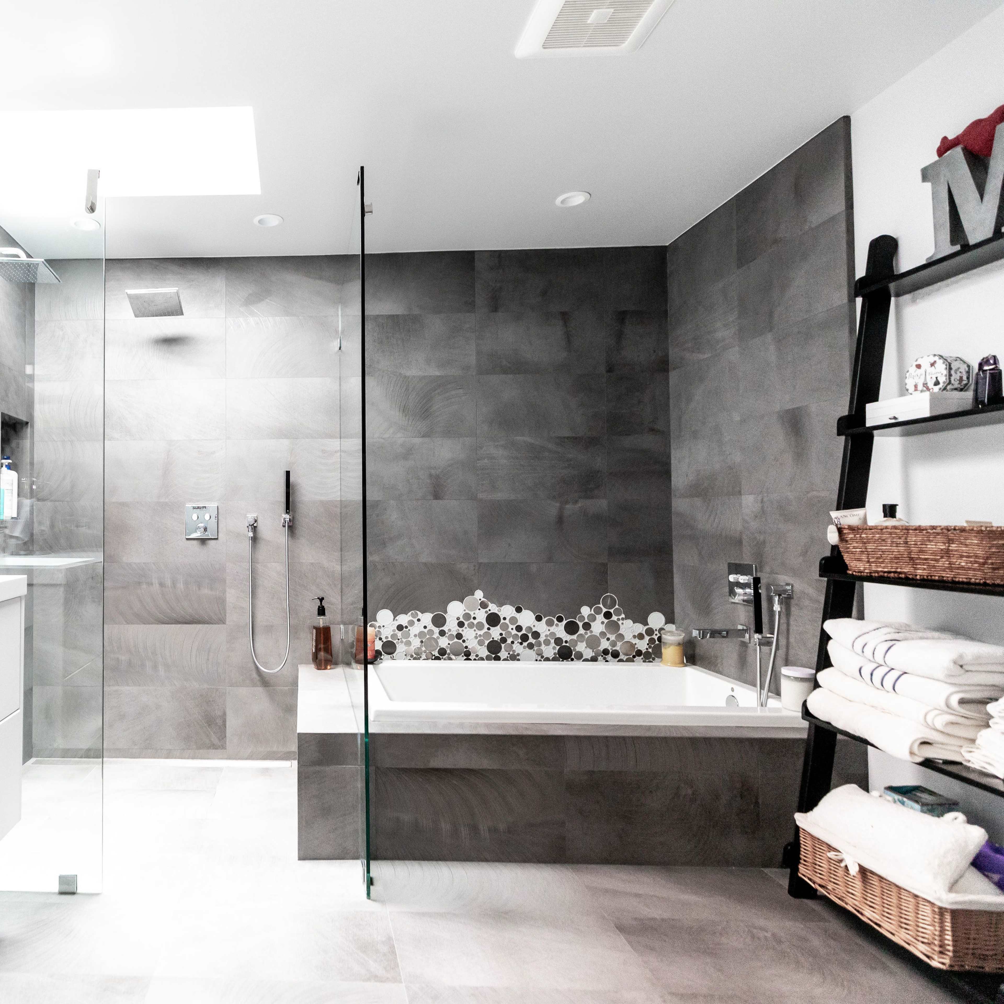A modern bathroom featuring a glass-enclosed shower, a freestanding bathtub, and a double sink vanity with a mosaic tile accent wall.
