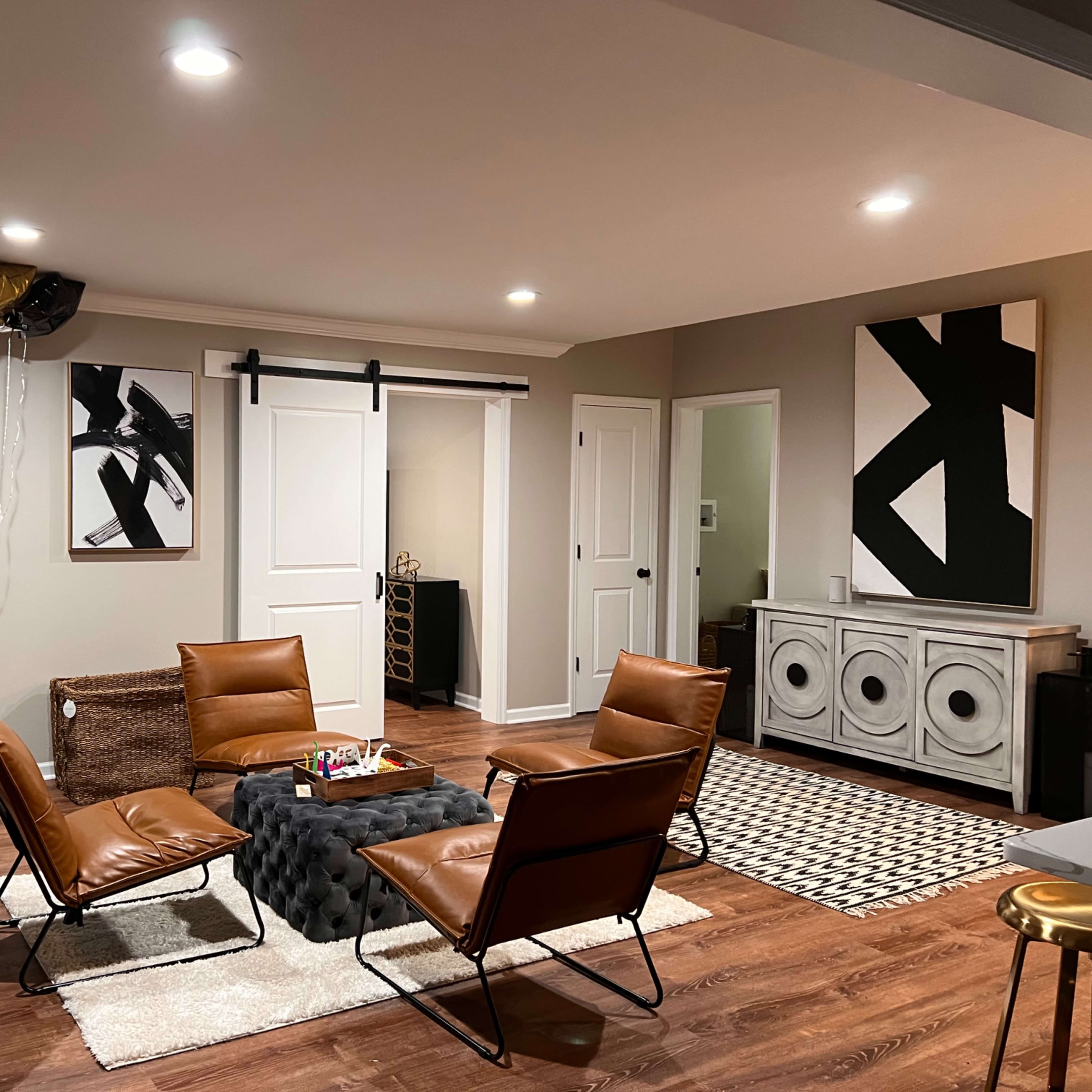 A modern living room with brown leather chairs arranged around a black coffee table, featuring abstract black-and-white art on the walls and decorative balloons in one corner.