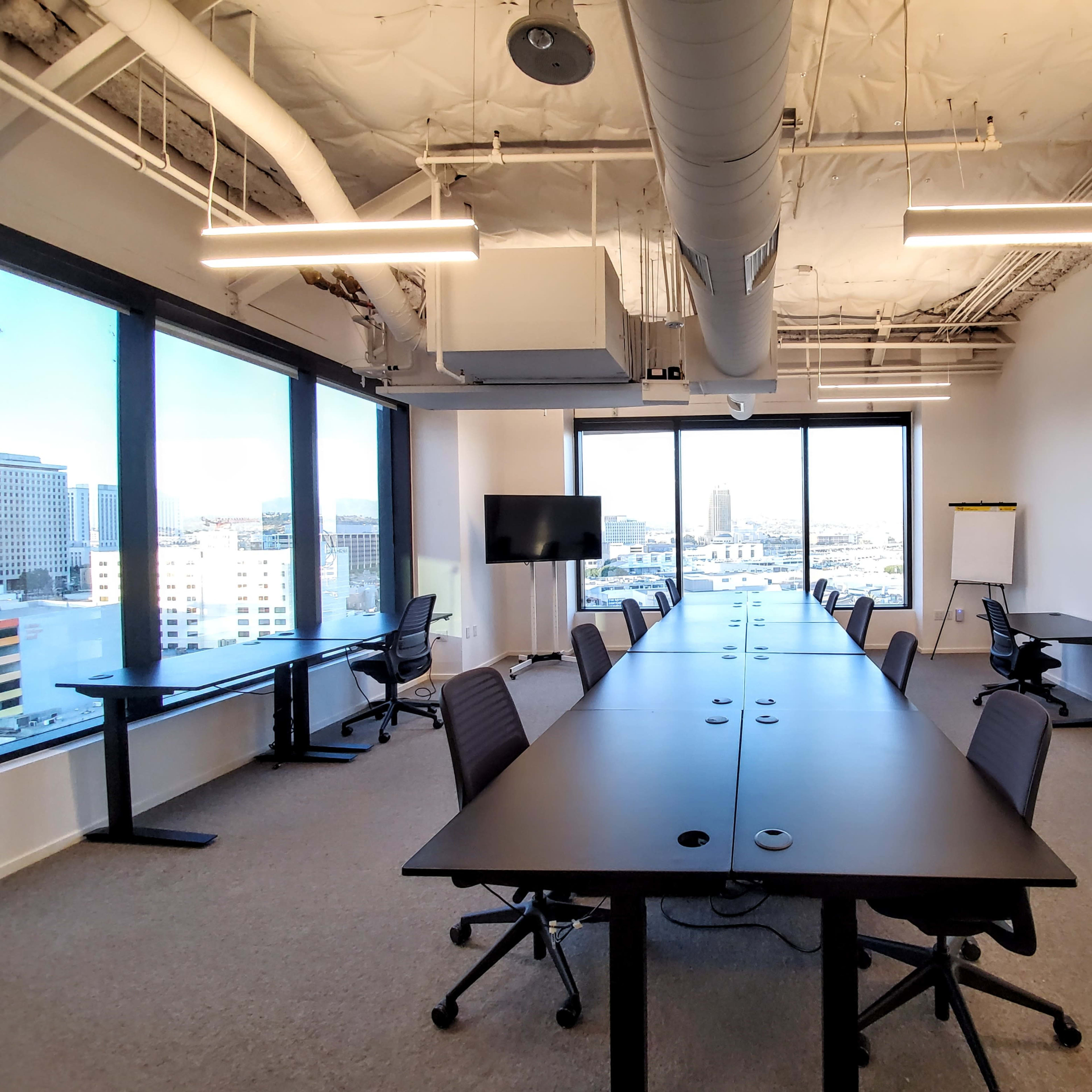 A modern conference room features multiple long tables with ergonomic chairs, large windows, and minimalistic decor.