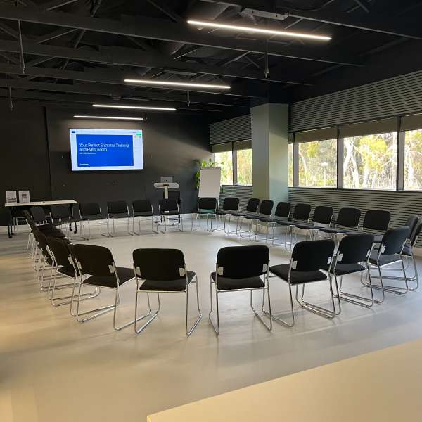 The room reset into a circle of chairs around the perimeter, a title slide on the screen.