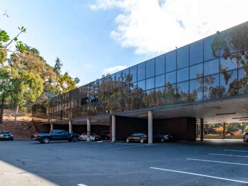 Covered parking spaces underneath the glass-fronted building.