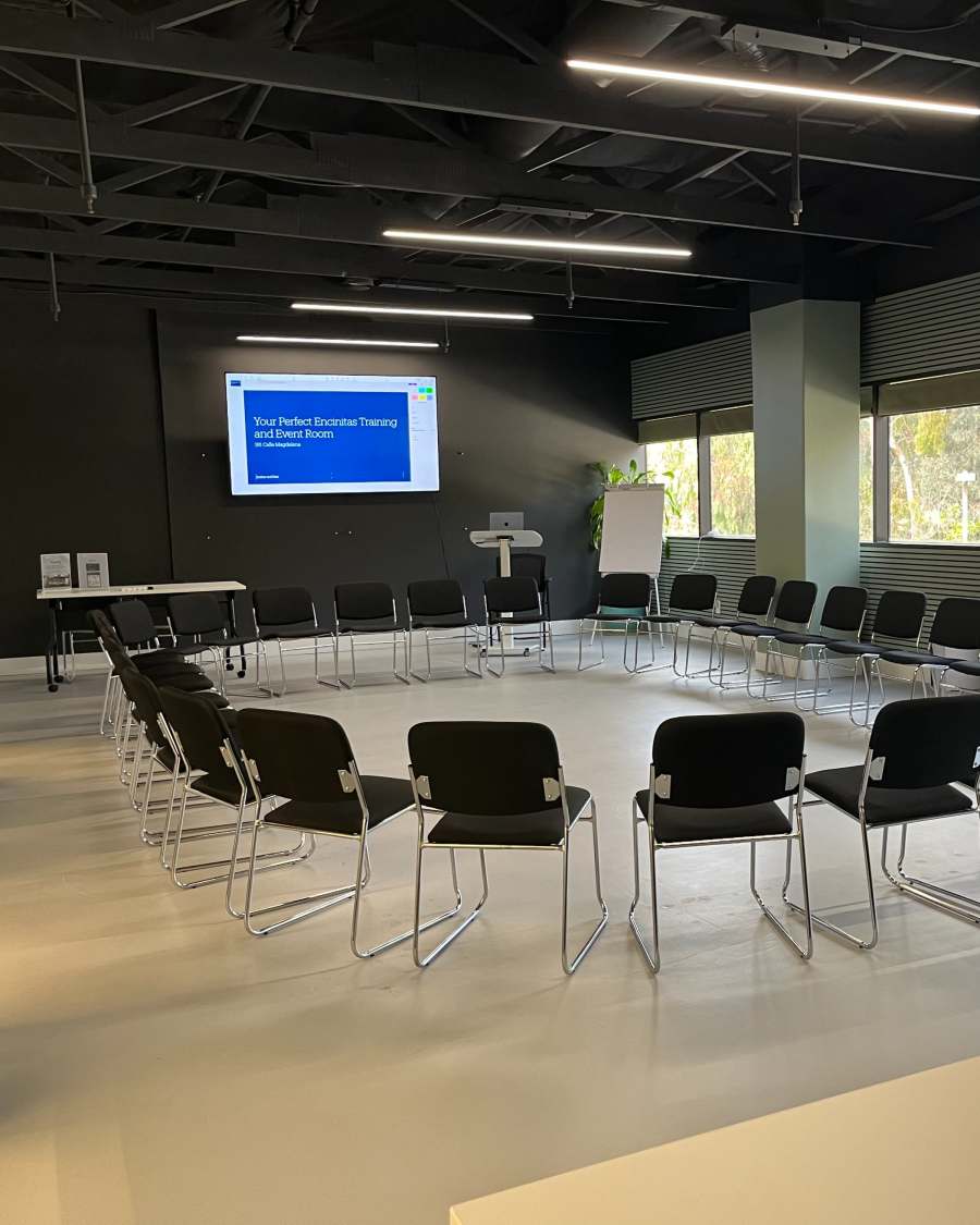 The room reset into a circle of chairs around the perimeter, a title slide on the screen.