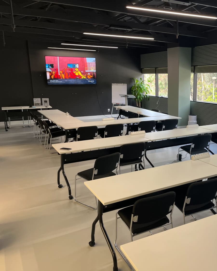 The training room with tables in a U-shape facing the screen, windows onto greenery.