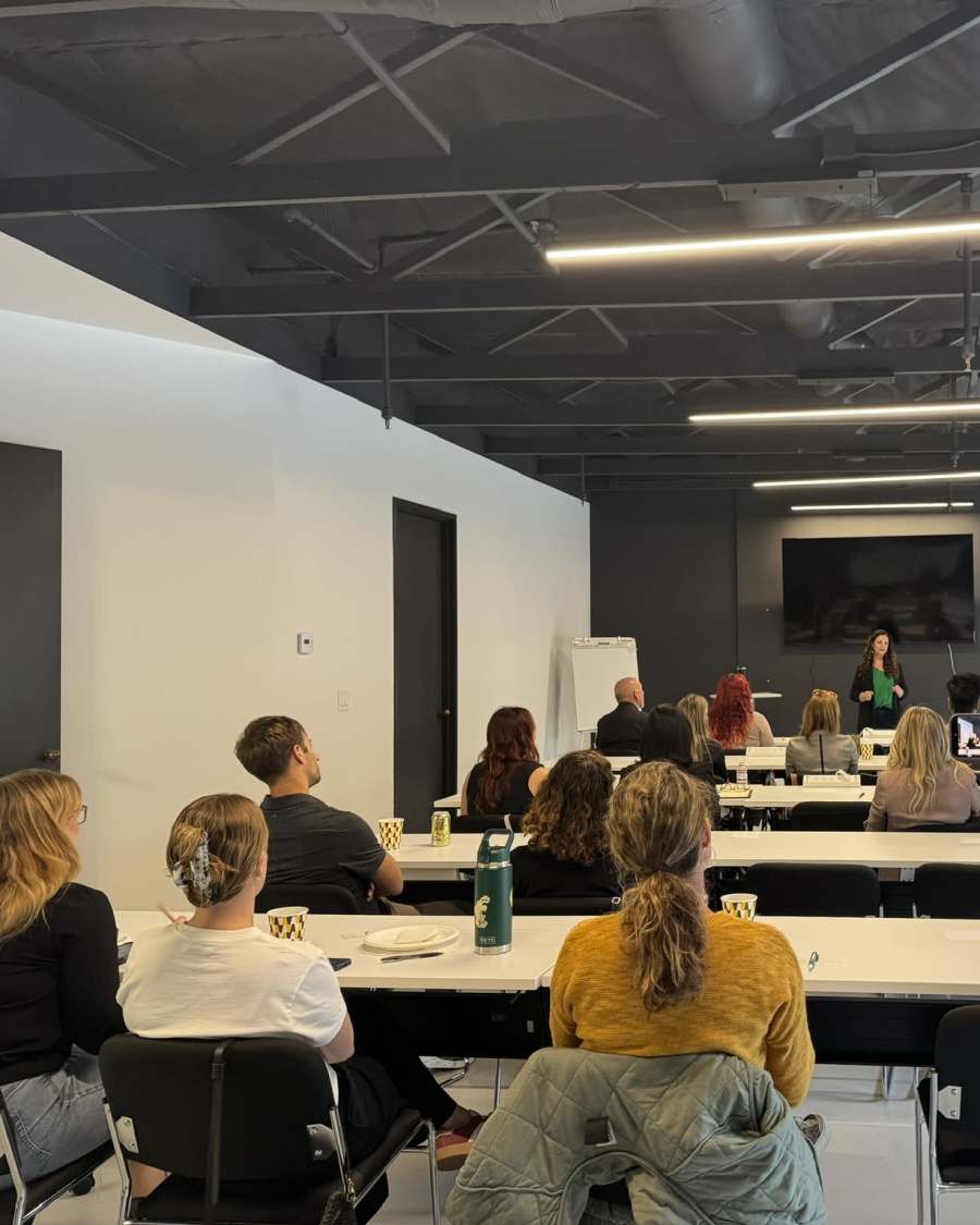 A group seated at tables turned toward a presenter at the front of the room.