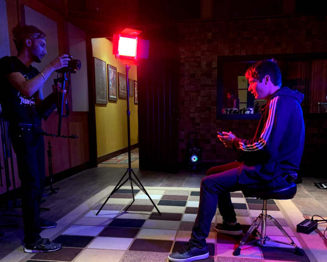 A photographer captures an individual seated on a stool, illuminated by a red light in a dimly lit room.