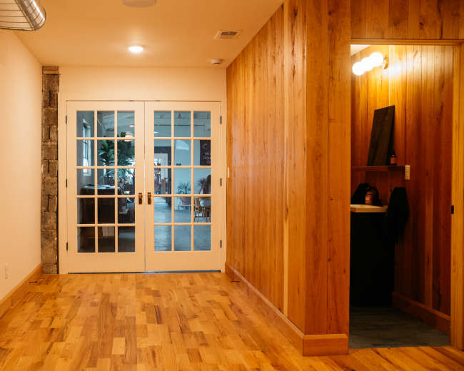 A hallway with wooden flooring leading to double glass doors and an adjacent wooden-paneled area.