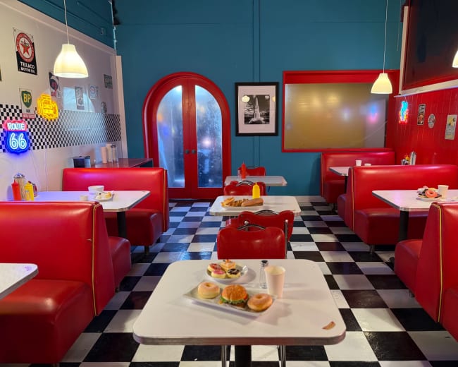 The image shows a retro diner interior with red booths, black and white checkered flooring, and a countertop displaying food items.