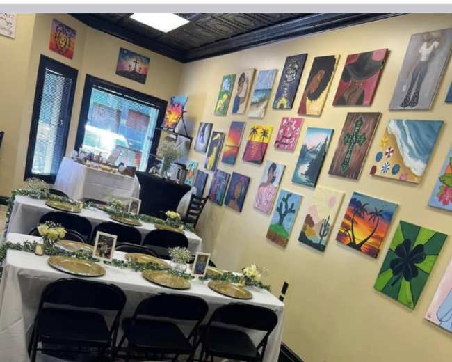A decorated dining area with multiple tables set for an event, featuring gold plates and floral centerpieces against a backdrop of colorful artwork on the walls.