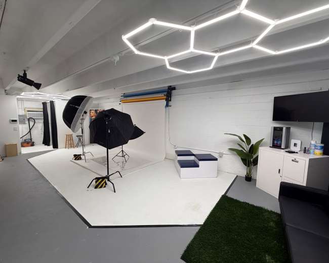 A photography studio features a backdrop, lighting equipment, a chair, a television, and artificial grass flooring.