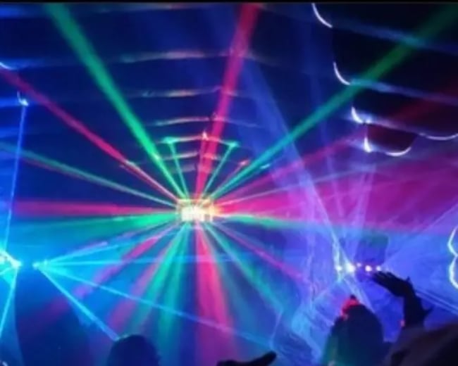 A crowd enjoys a vibrant lightshow with colorful laser beams illuminating a dimly lit space.